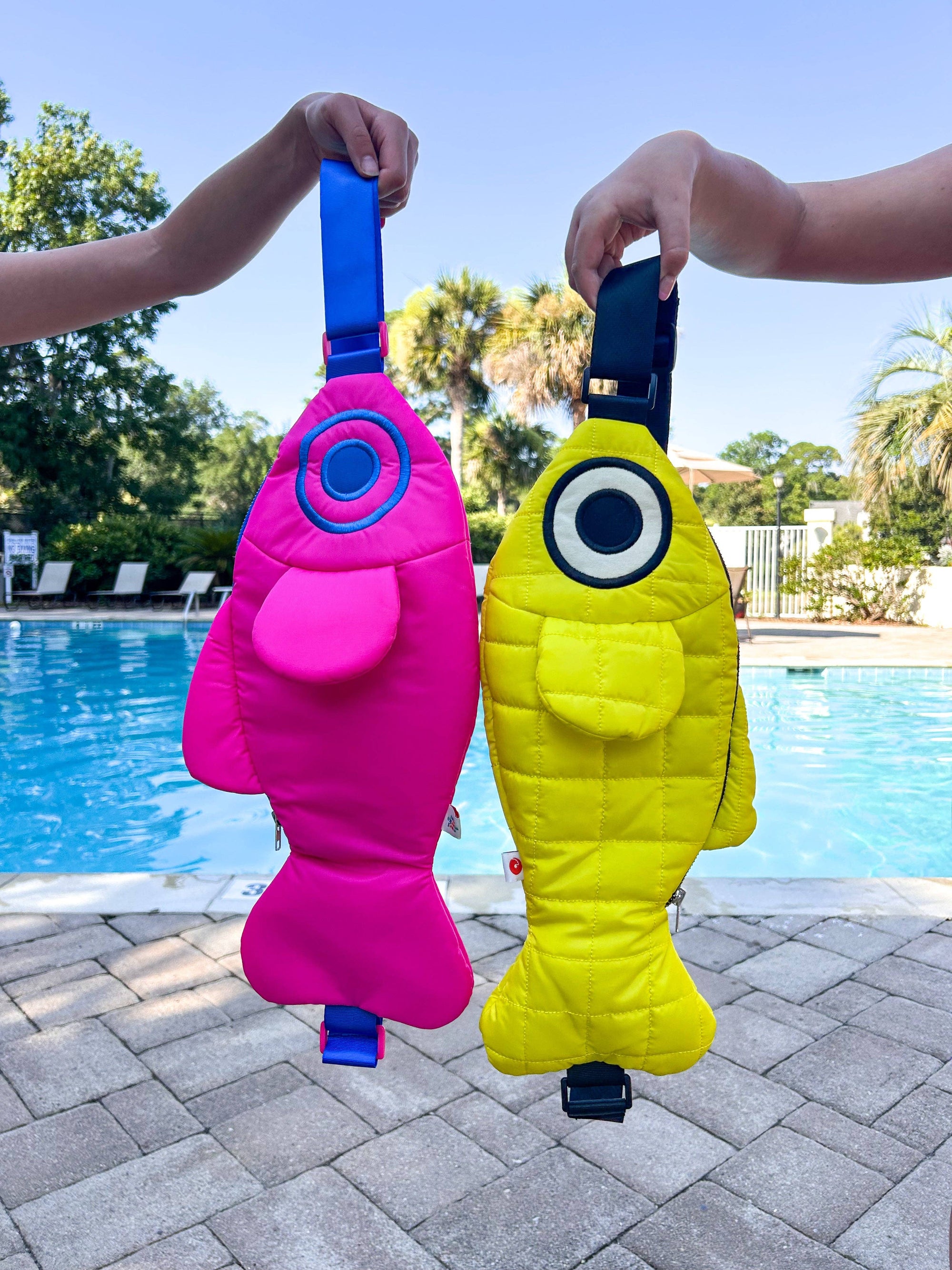 Two colorful bags, one pink and one yellow, held by people by a pool.
