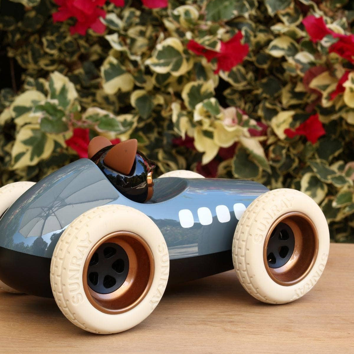 Toy car with a small figure inside on a wooden surface with a floral background
