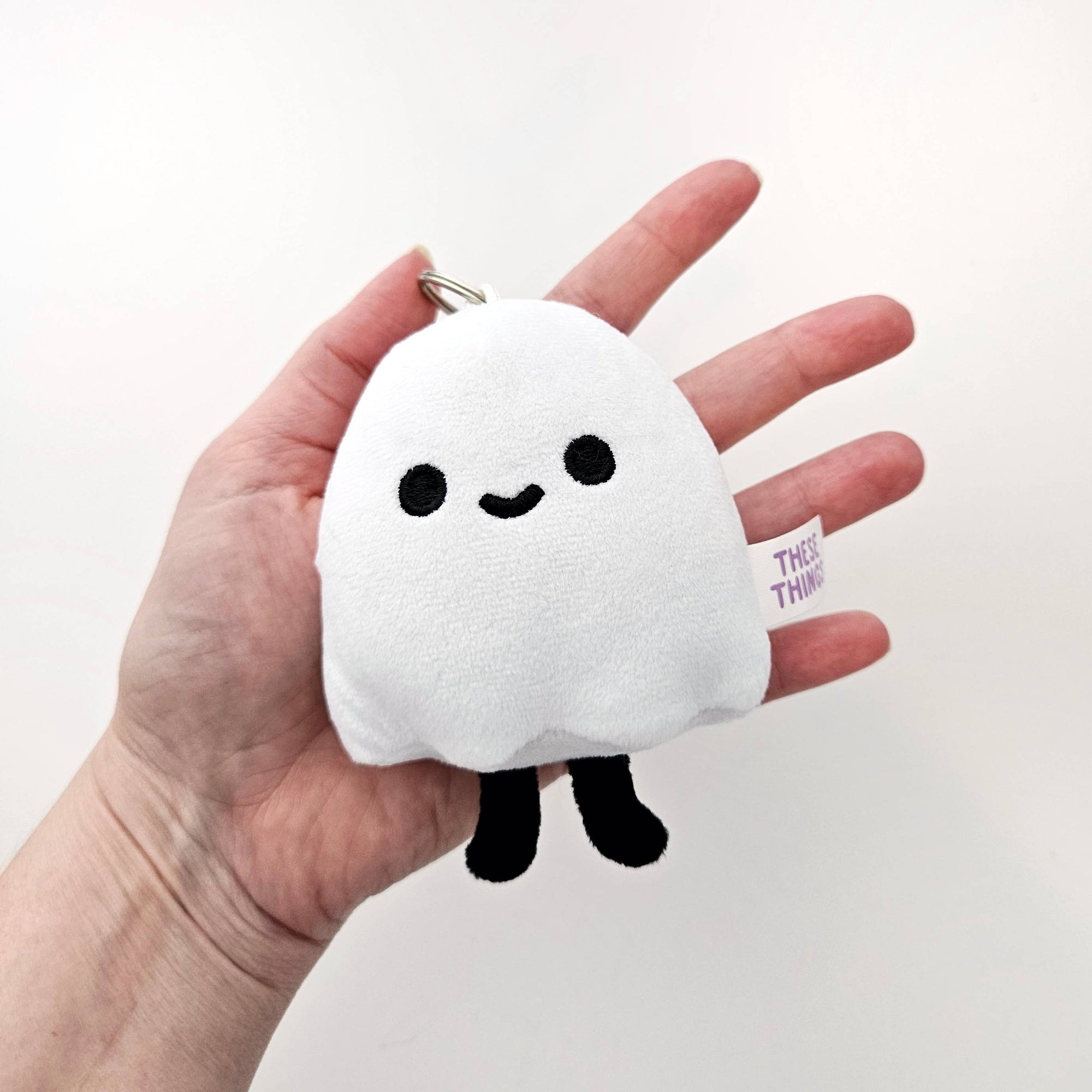 White plush cloud keychain with black eyes and legs held in a hand against a white background
