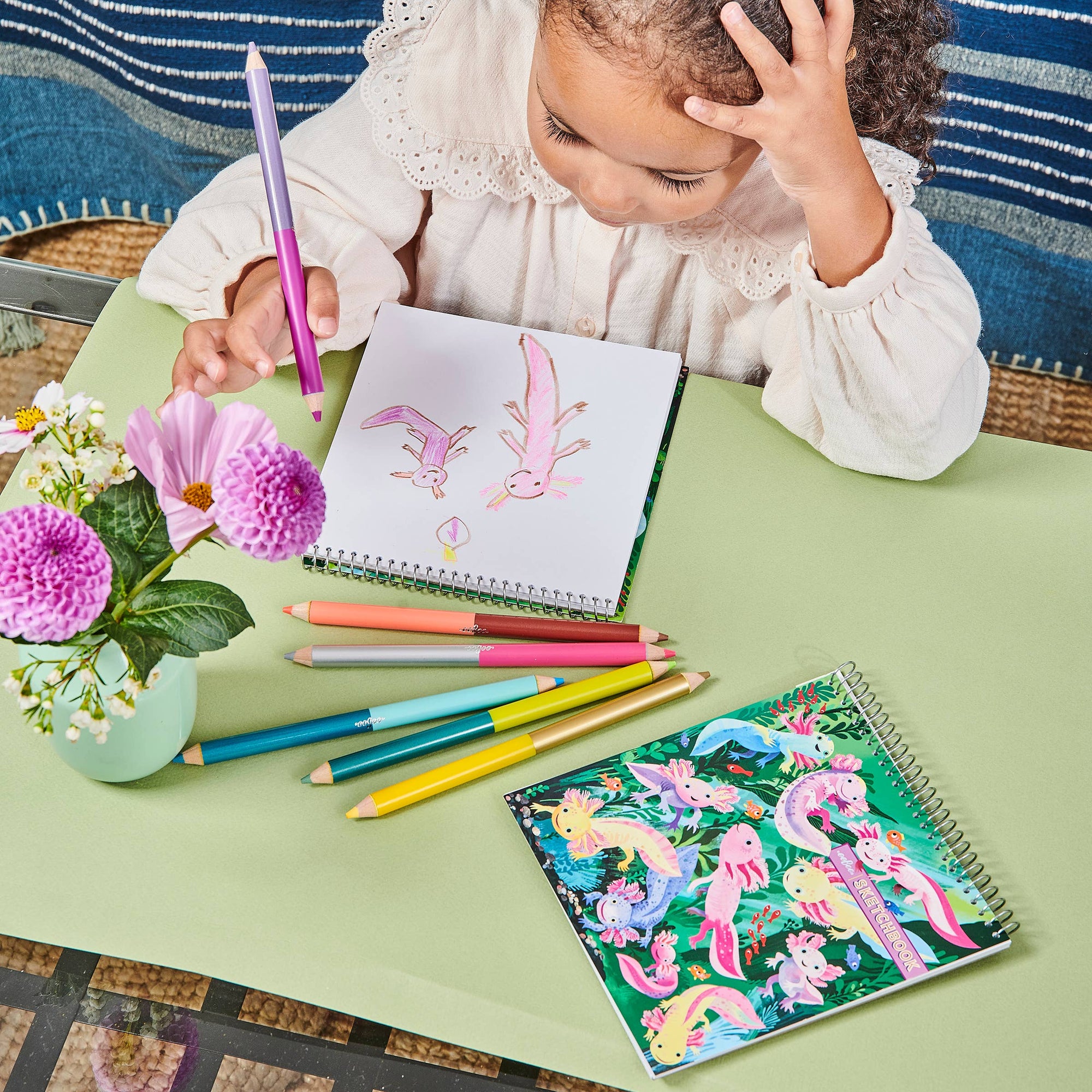 Child coloring with a coloring book and pencils on a green table