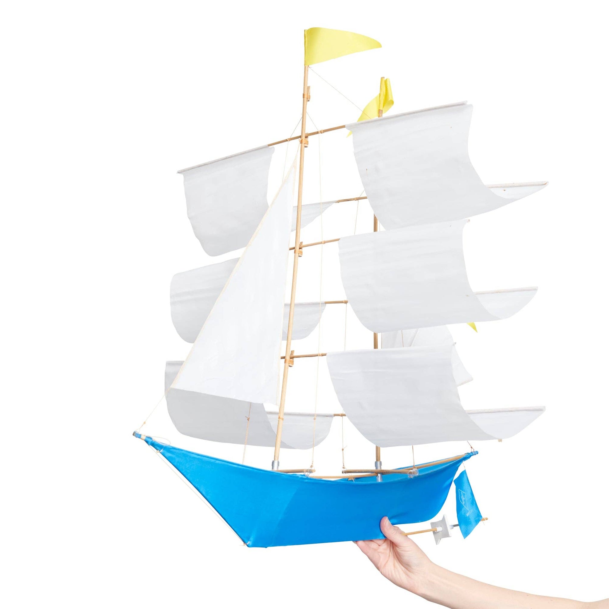 Model sailboat with white sails and a blue hull held by a hand on a white background