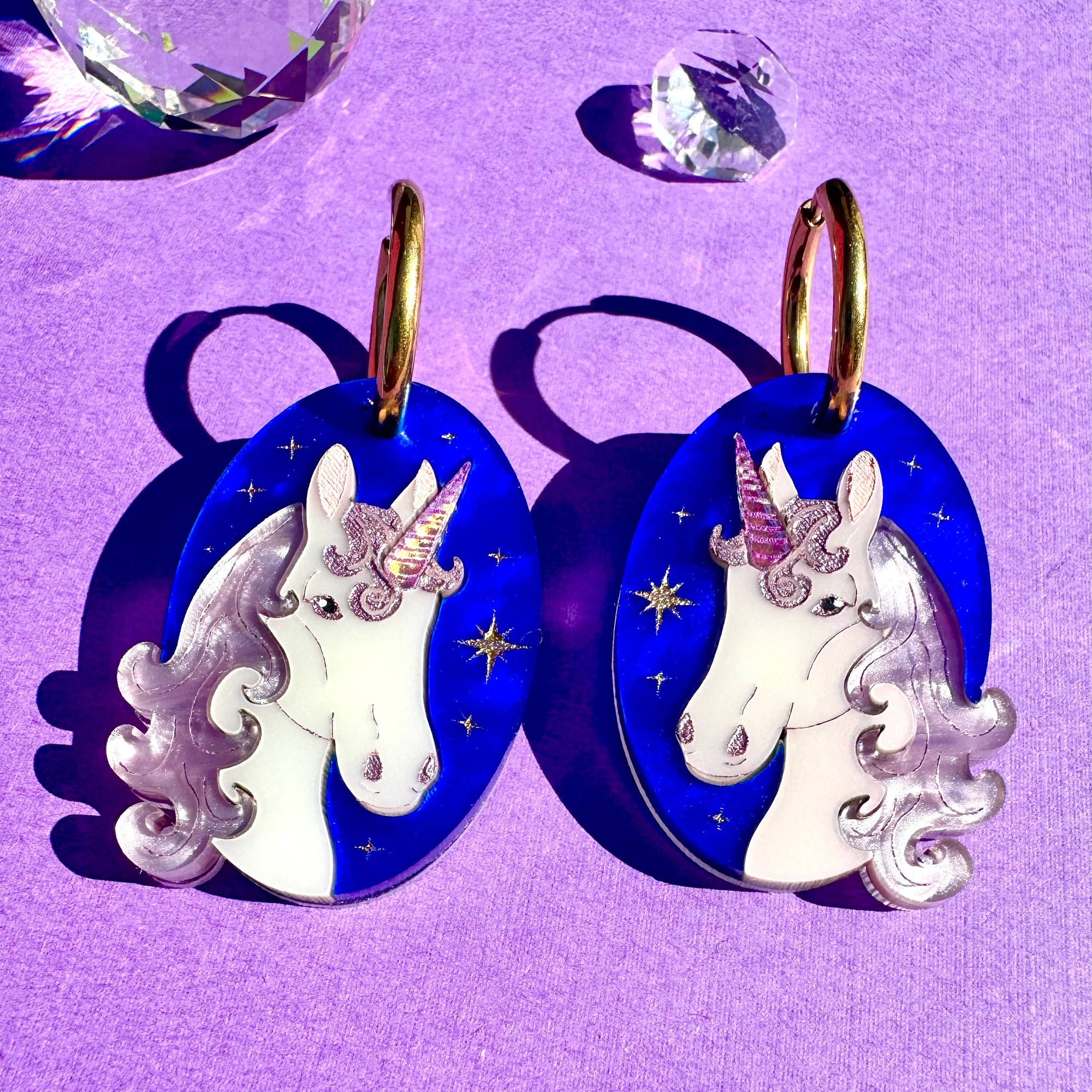 Unicorn-shaped earrings on a purple background with crystals.