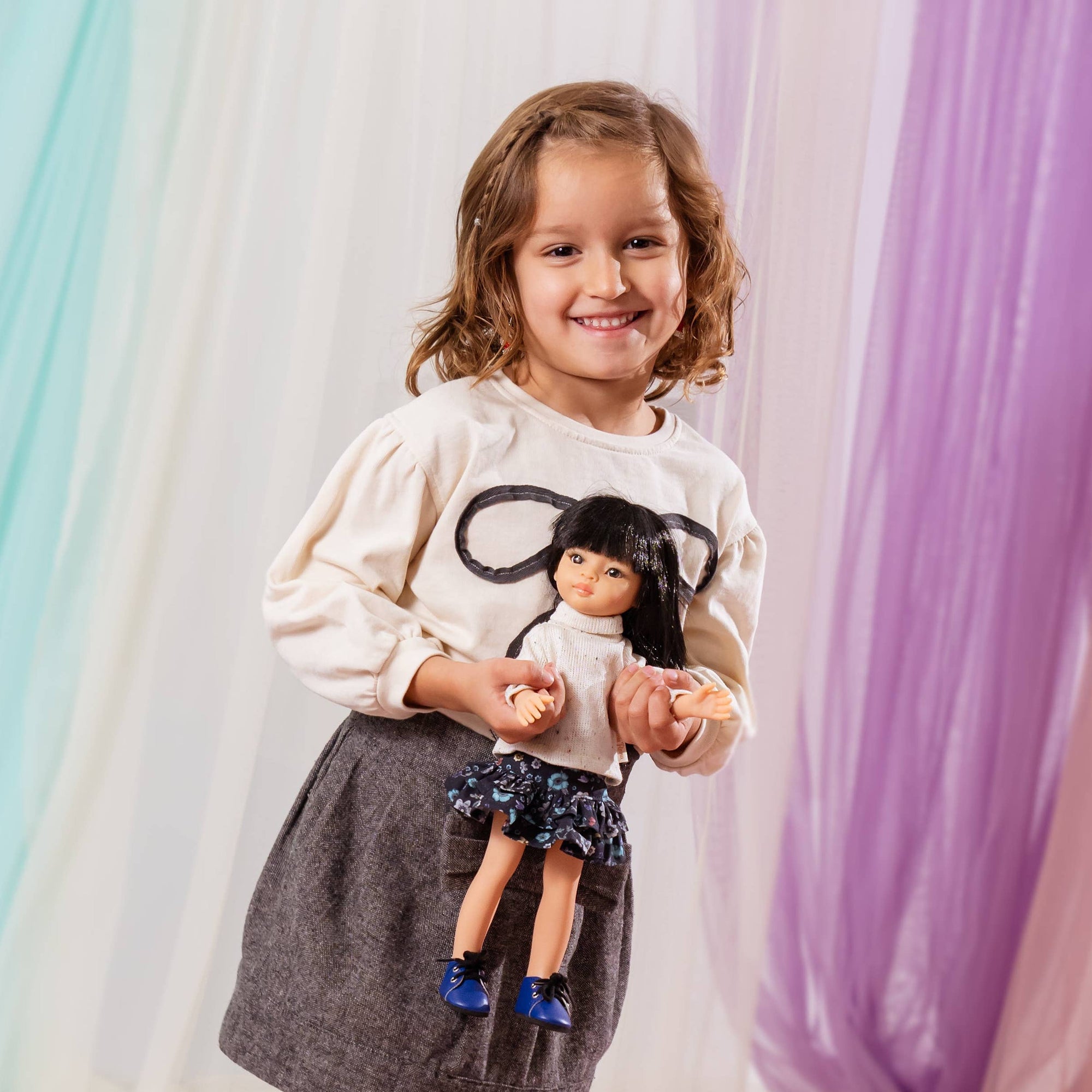 Young girl holding a doll against a colorful curtain backdrop