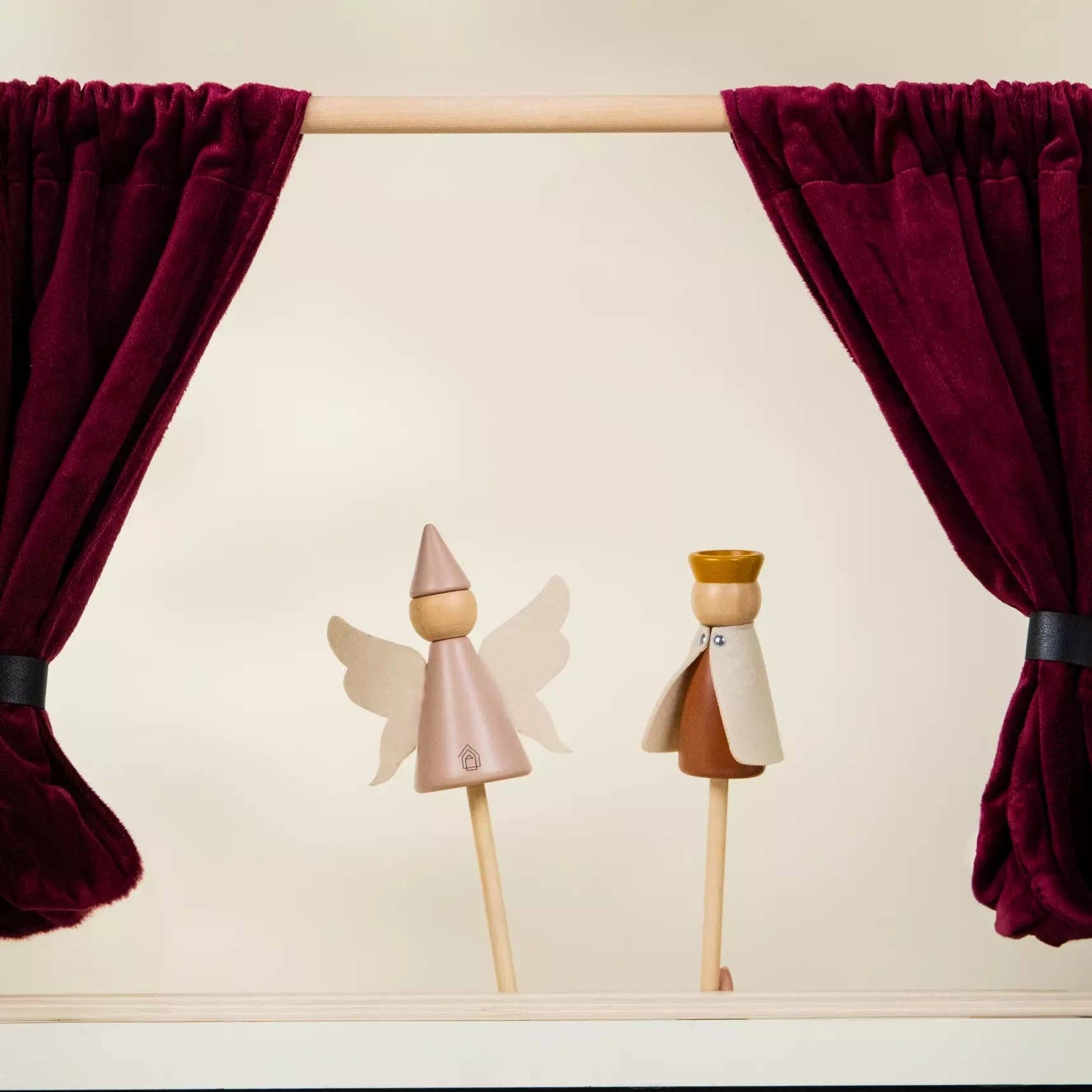 Two wooden puppets on sticks in front of red velvet curtains.