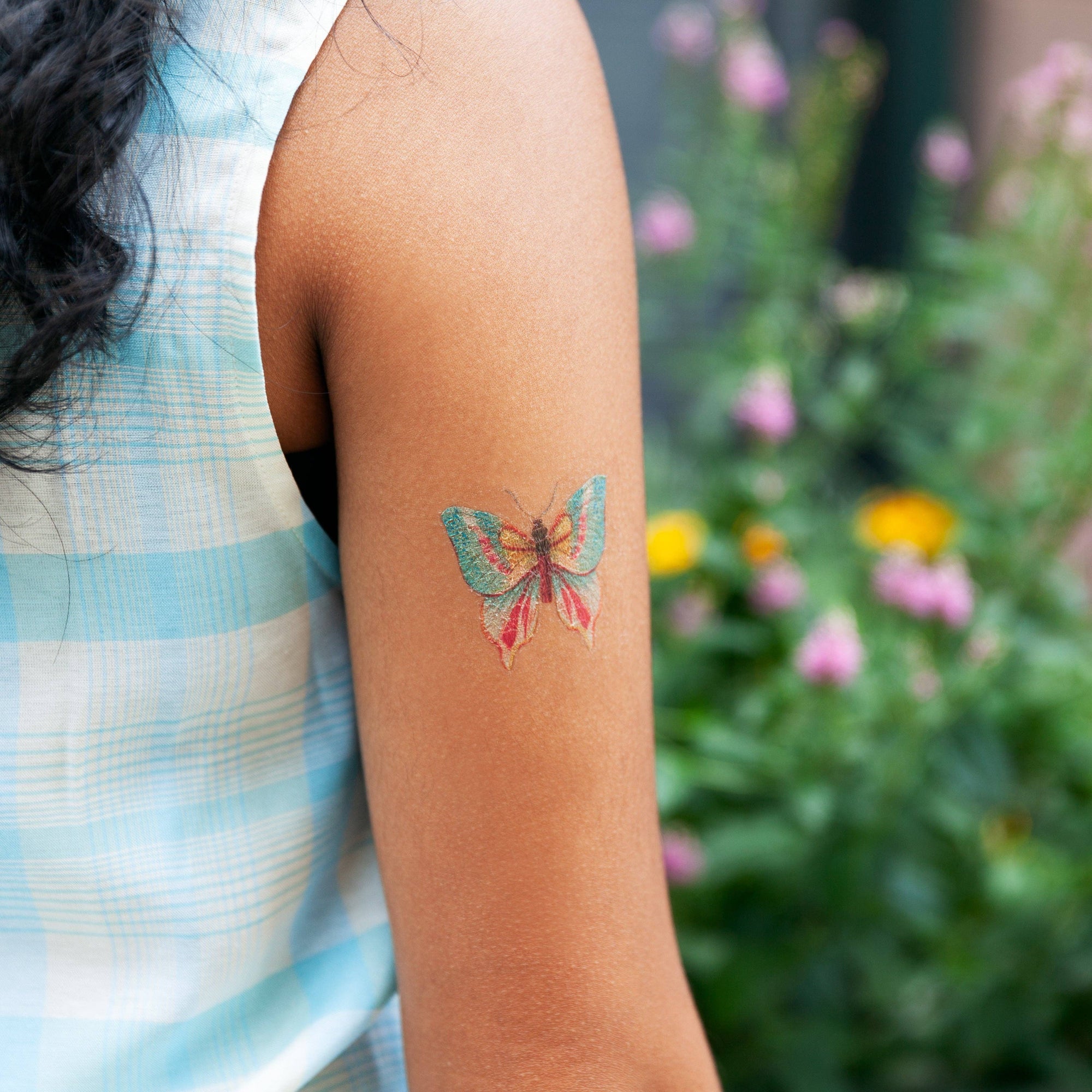 Tattoo of a colorful butterfly on a person's arm with a blurred natural background