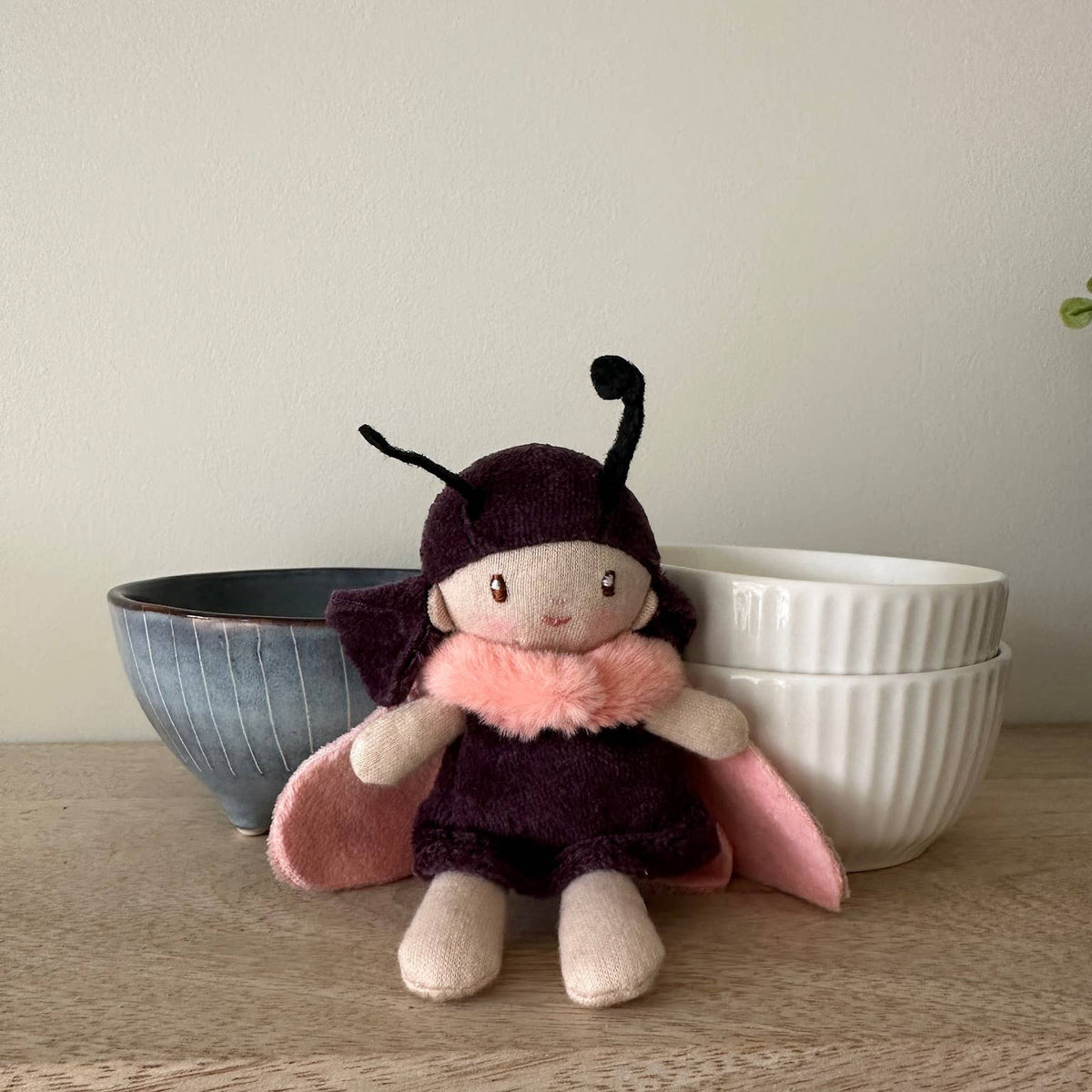 Stuffed toy in a butterfly costume on a wooden surface with bowls in the background
