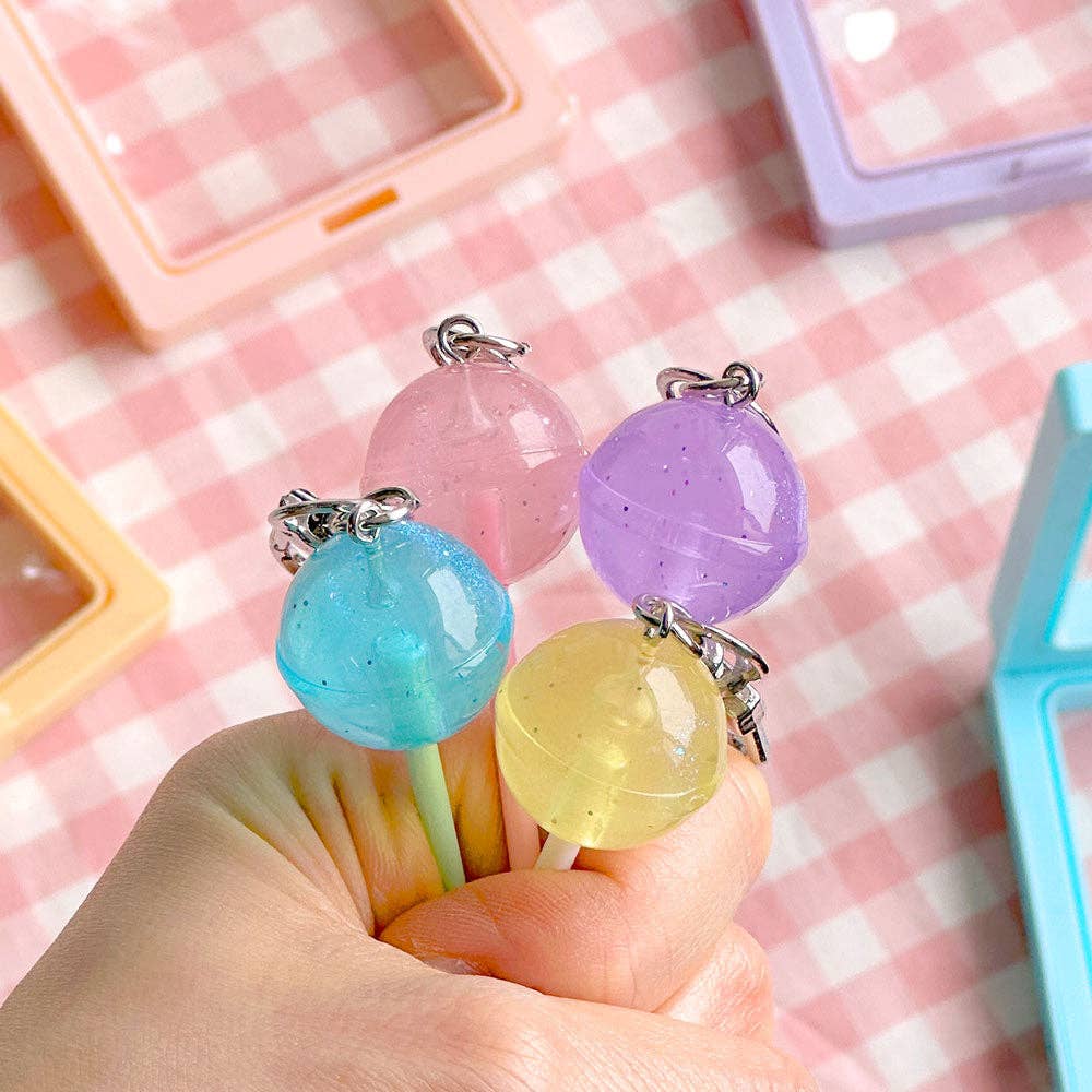 Colorful lollipop-shaped keychains held by a hand on a pink checkered background