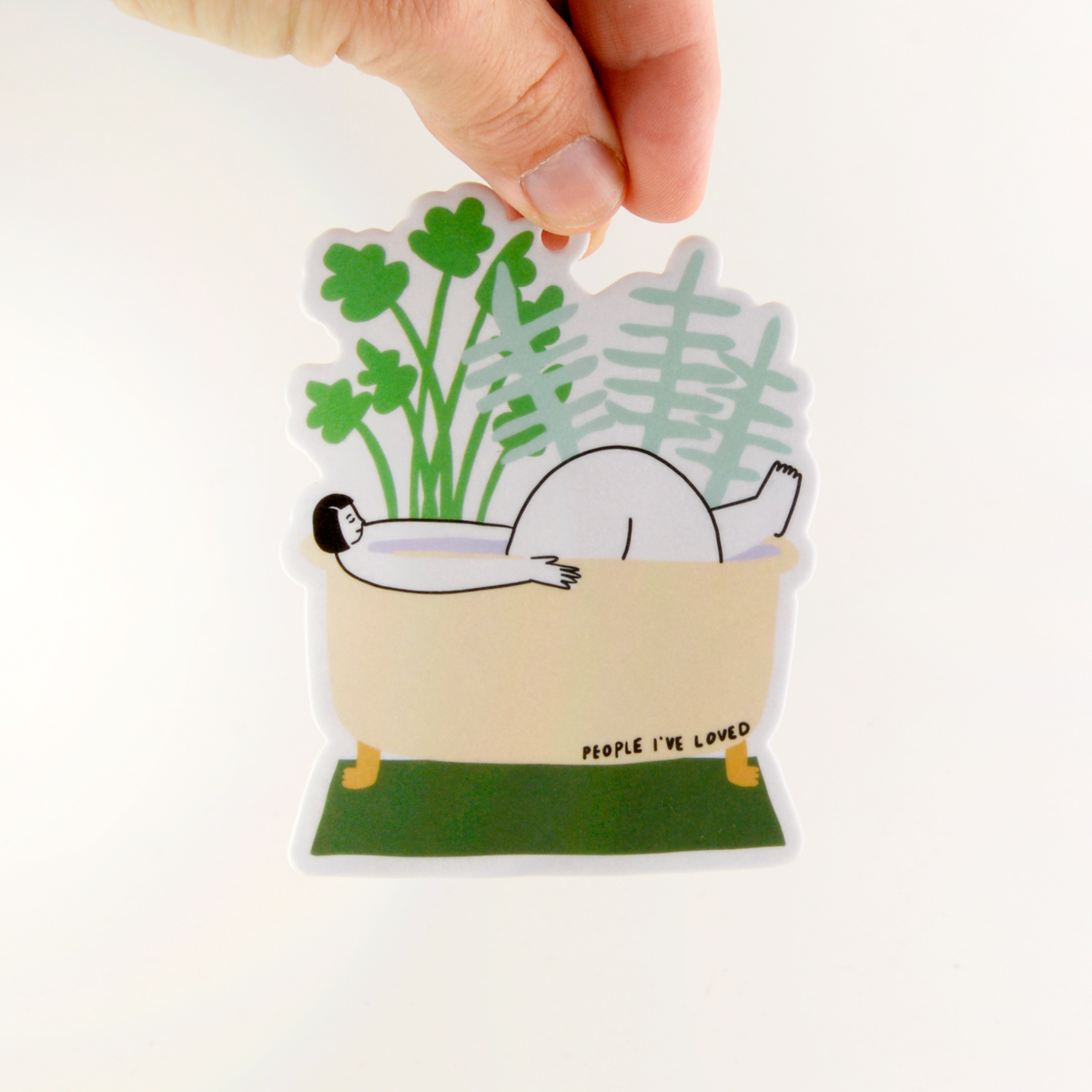 Sticker of a person lying in a garden with plants, held by a hand on a white background.