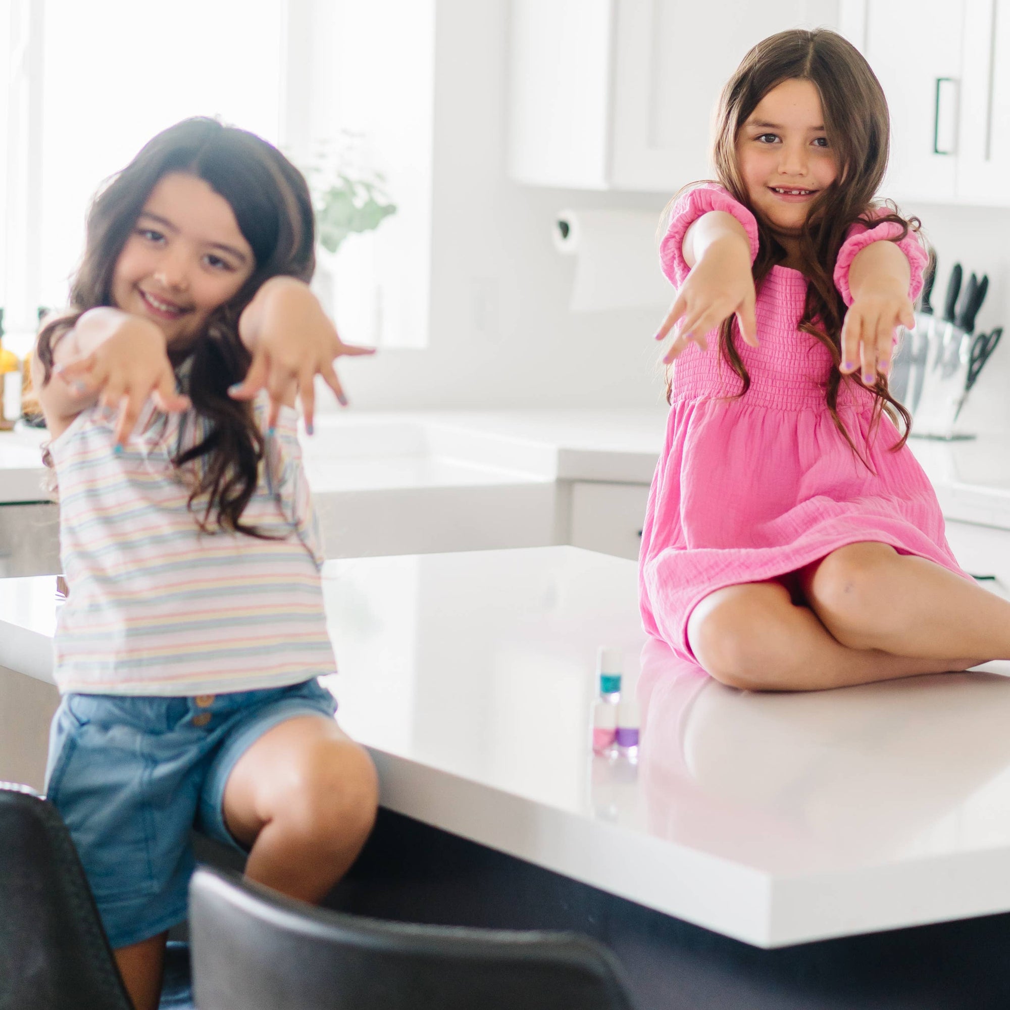 Two young girls sitting on a kitchen counter, smiling at the camera.