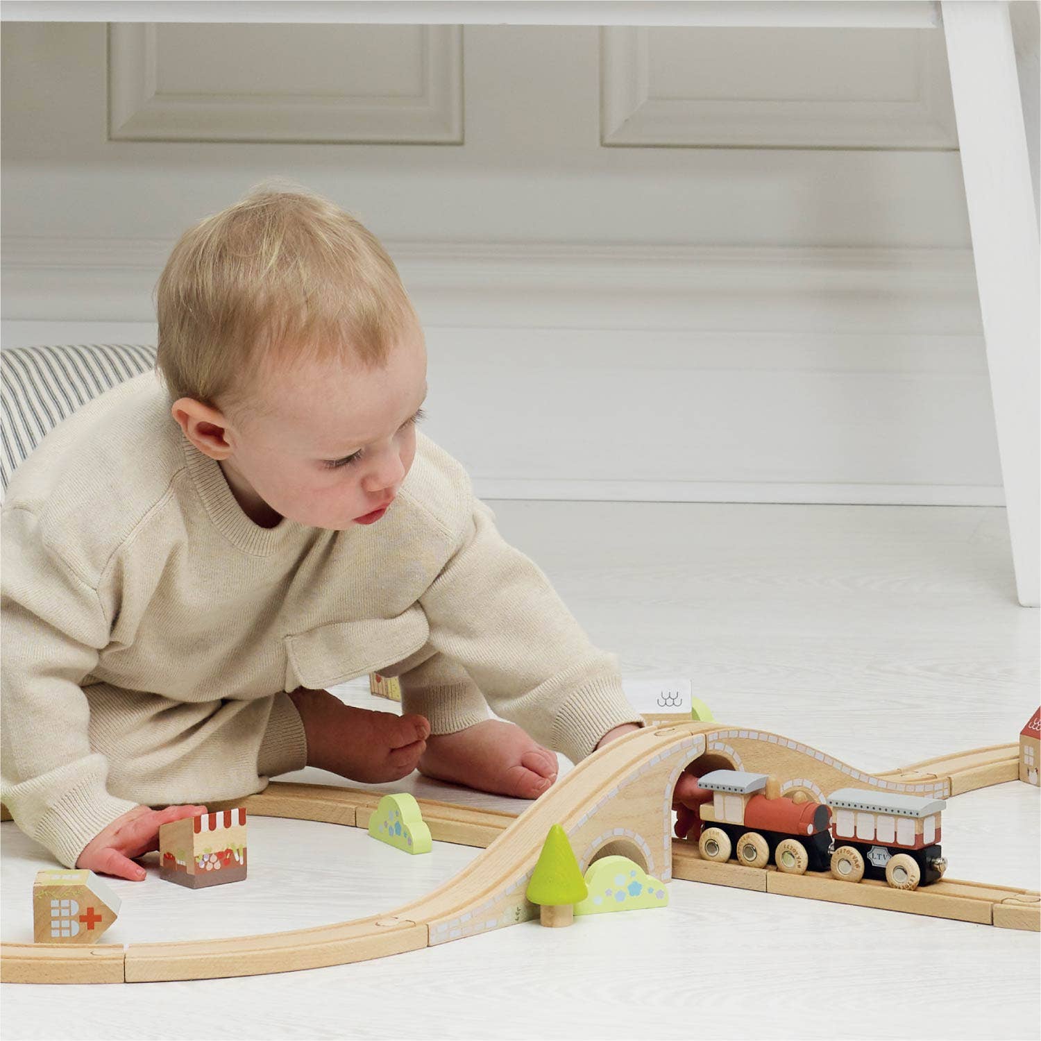 Child playing with a wooden train set on a light-colored floor.