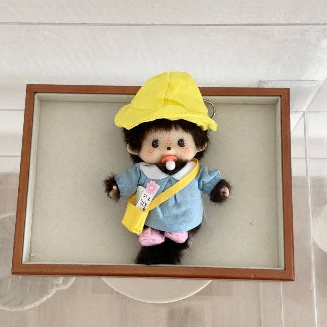 Stuffed monkey toy in a yellow outfit inside a wooden frame on a light background