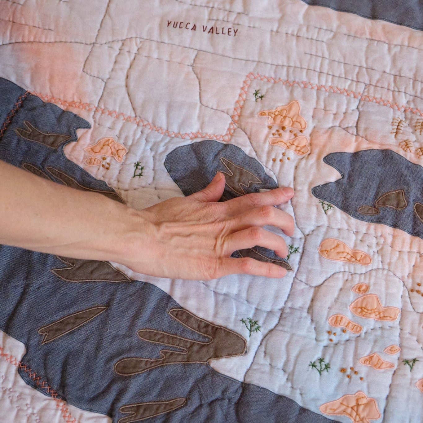 Hand touching a quilt with embroidered designs on a bed.