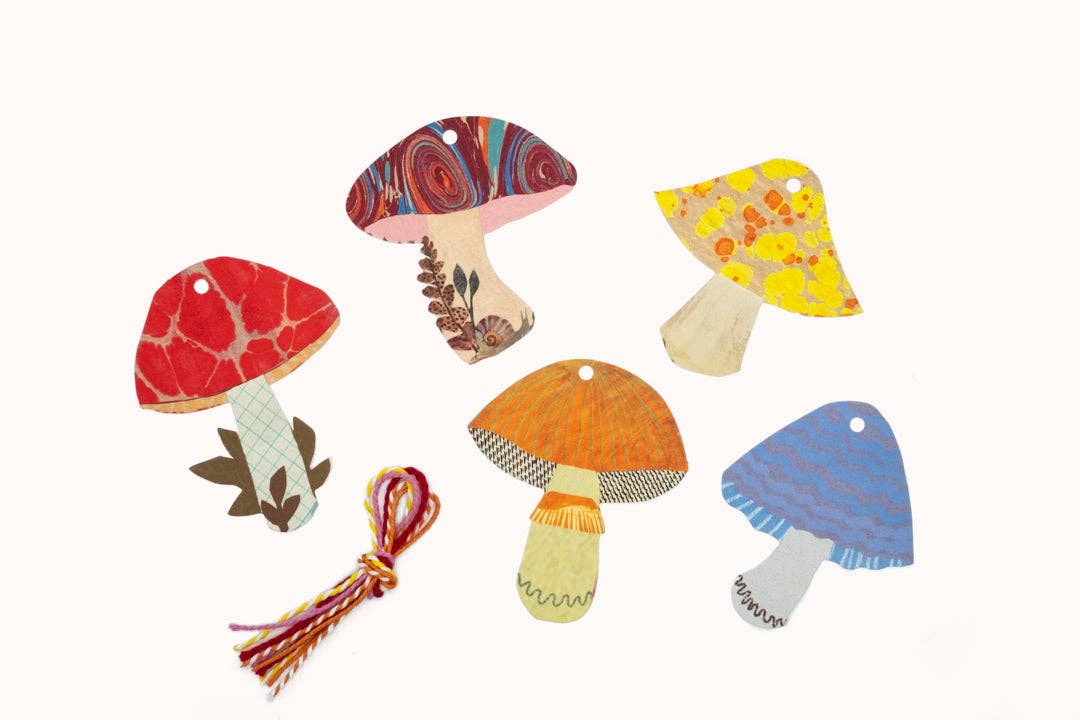 Six colorful mushroom-shaped decorative tags or ornaments with embroidered patterns and hanging holes, arranged on a plain off-white background.
