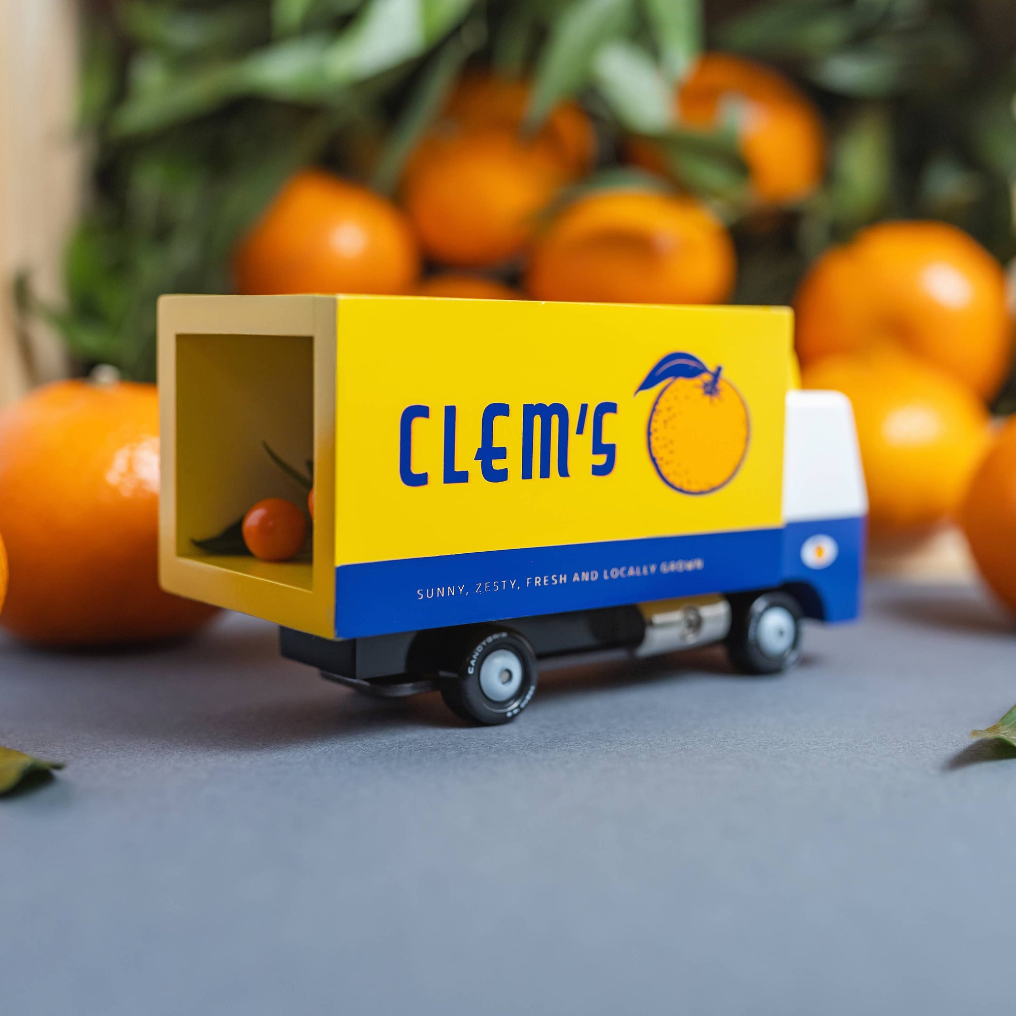 Toy truck with 'Clem's' branding surrounded by oranges on a gray surface.