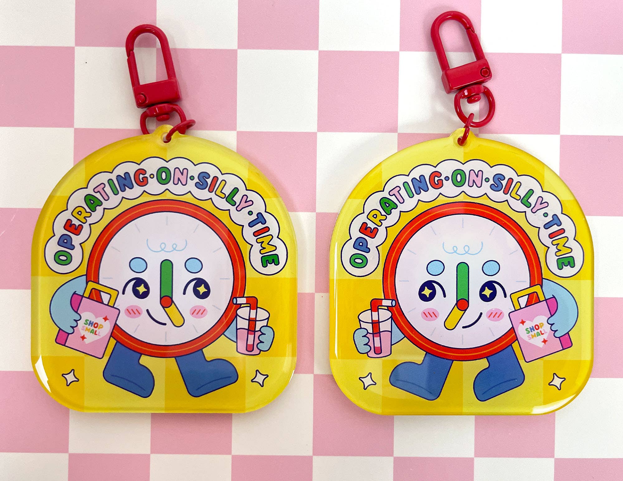 Two yellow keychains with a cartoon character on a pink and white checkered background
