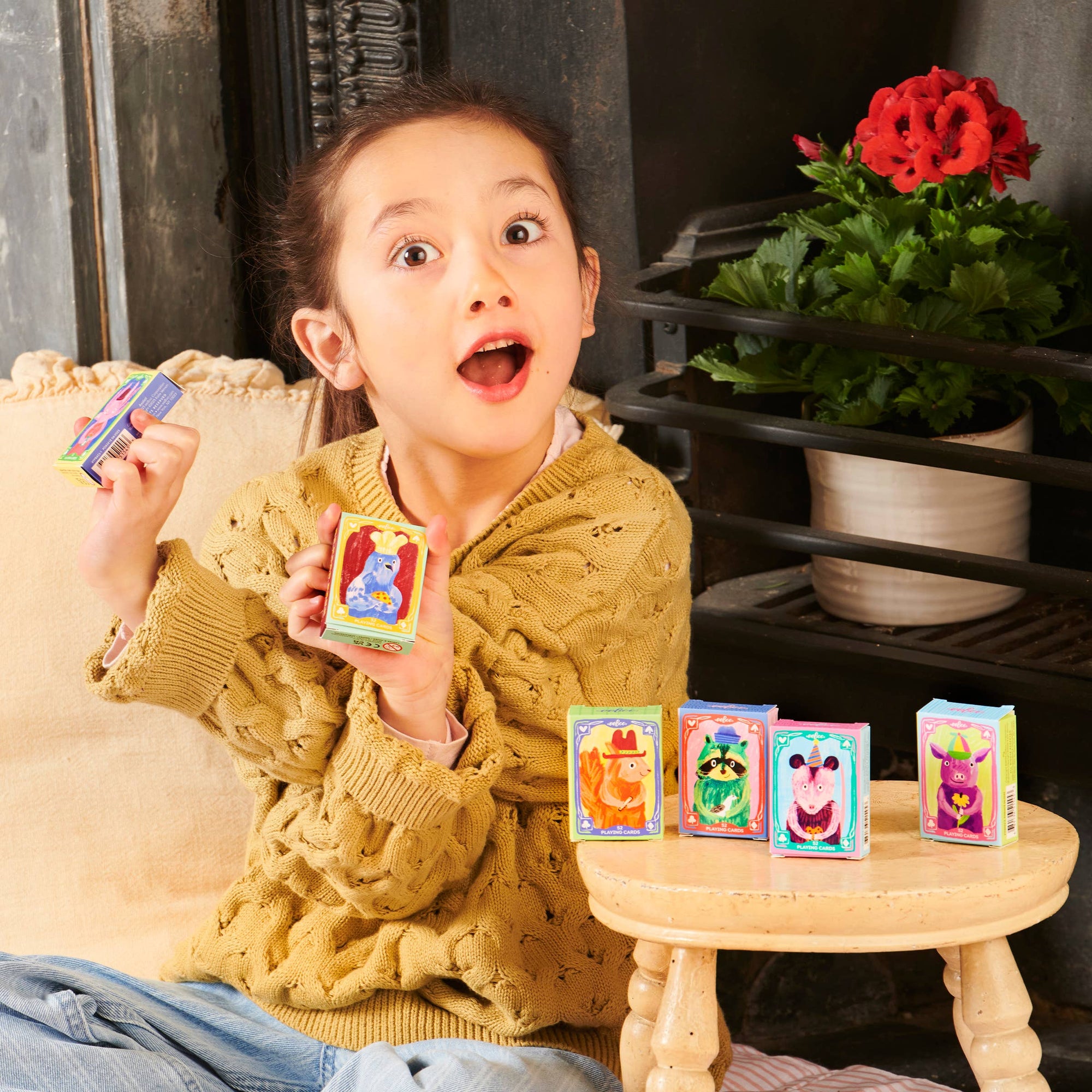 Child holding colorful trading cards in a cozy indoor setting with plants.