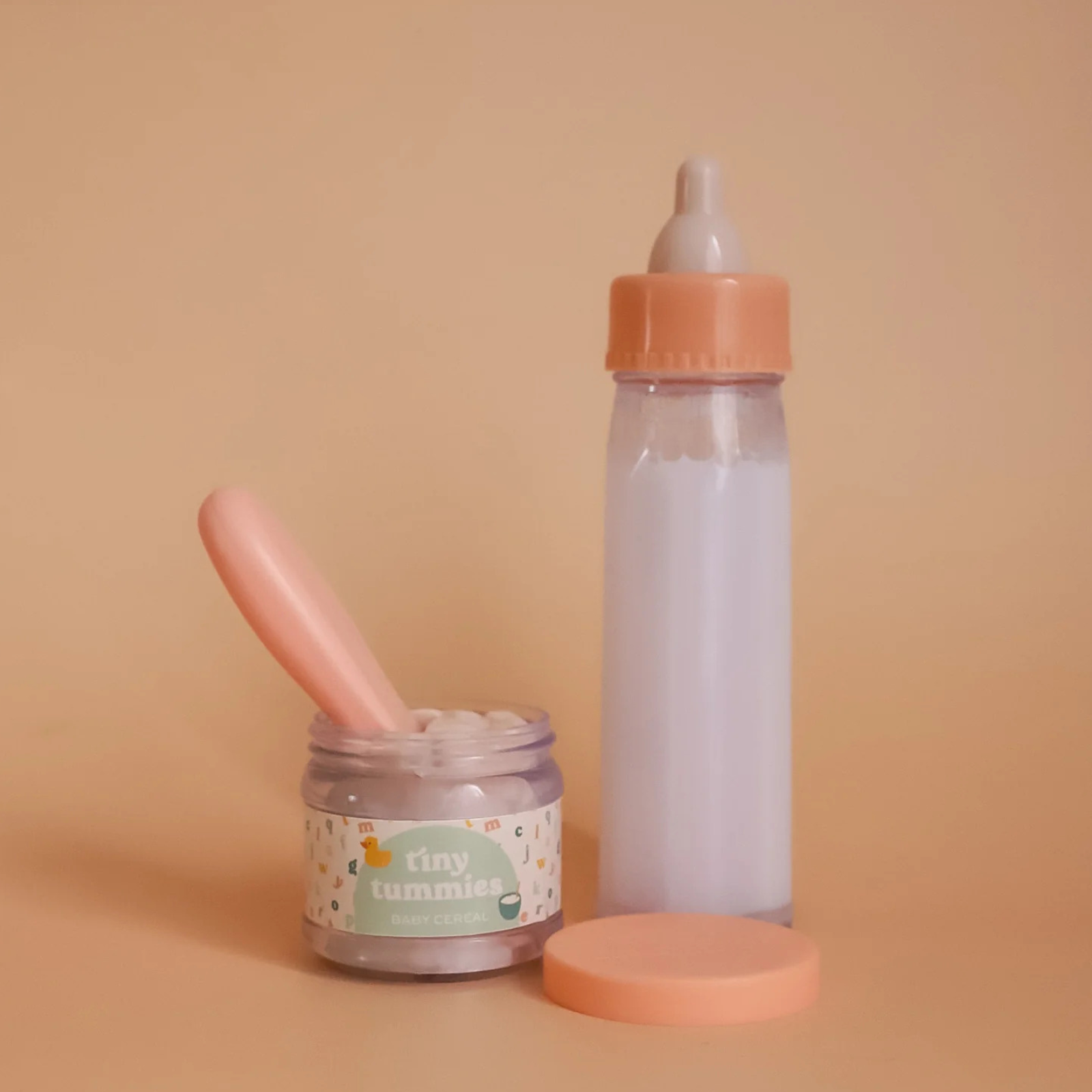 Baby bottle, jar, and spoon on a beige background with 'tiny tummies' branding.