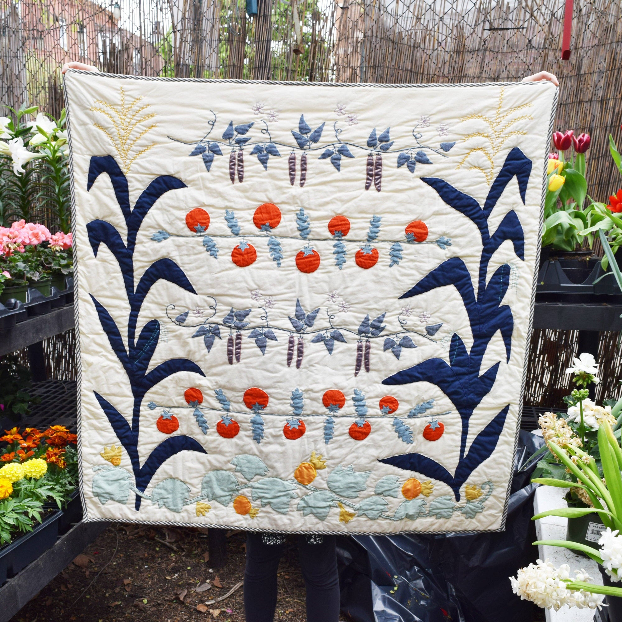 Quilt with floral patterns held up against a garden background
