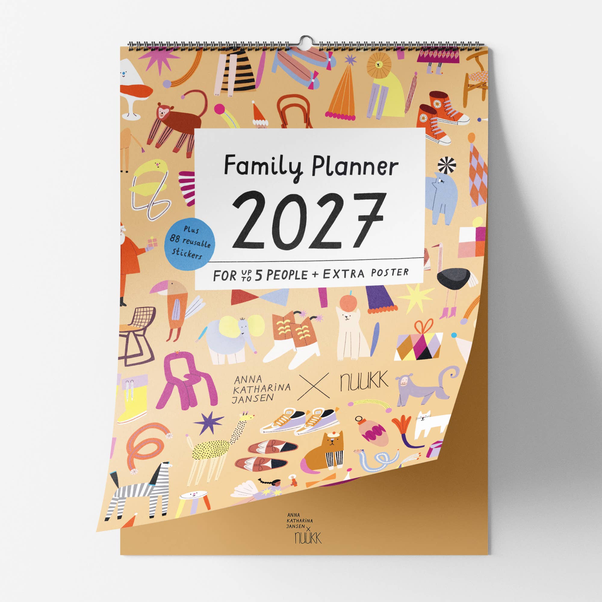 A spiral-bound 2027 Family Planner by Anna Katharina Dansen x Nukk, featuring a beige cover decorated with colorful whimsical illustrations and a gold-toned base, shown against a light gray background.