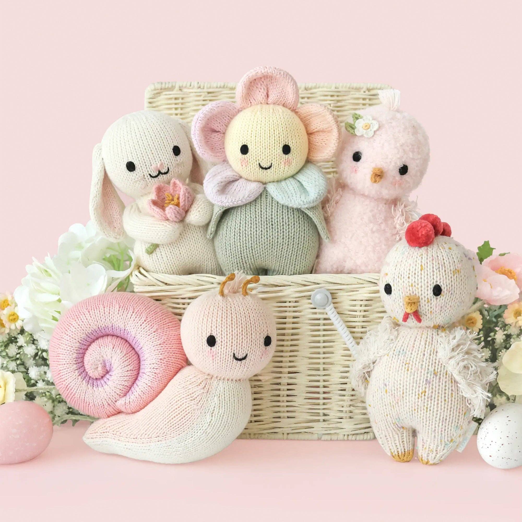 Set of knitted toys including a rabbit, elephant, and chicken in a basket on a pink background.