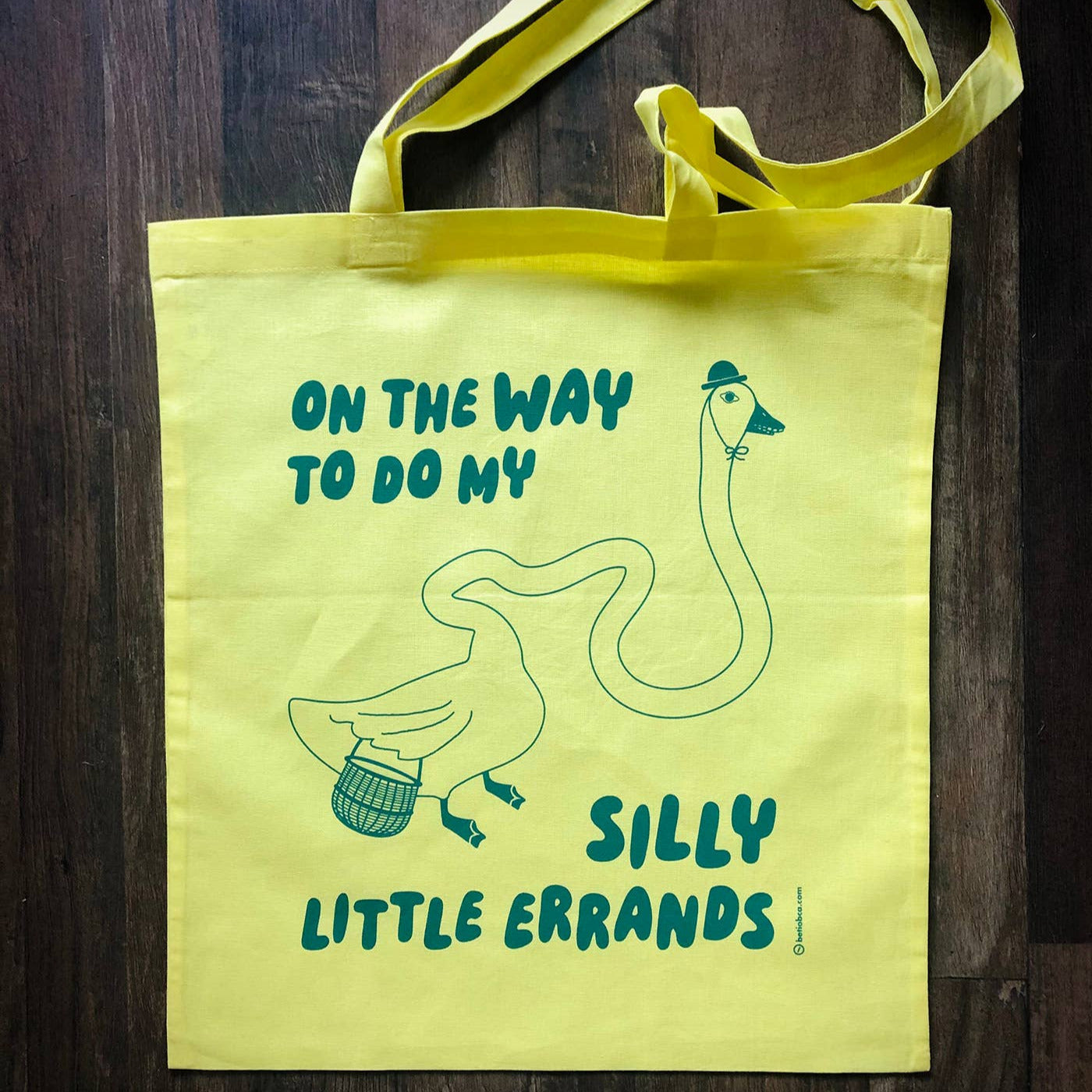 Yellow tote bag with a duck illustration and text on a wooden surface