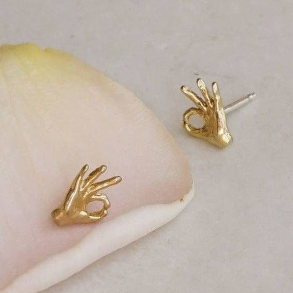 Gold hand-shaped earrings on a pink petal with a light background