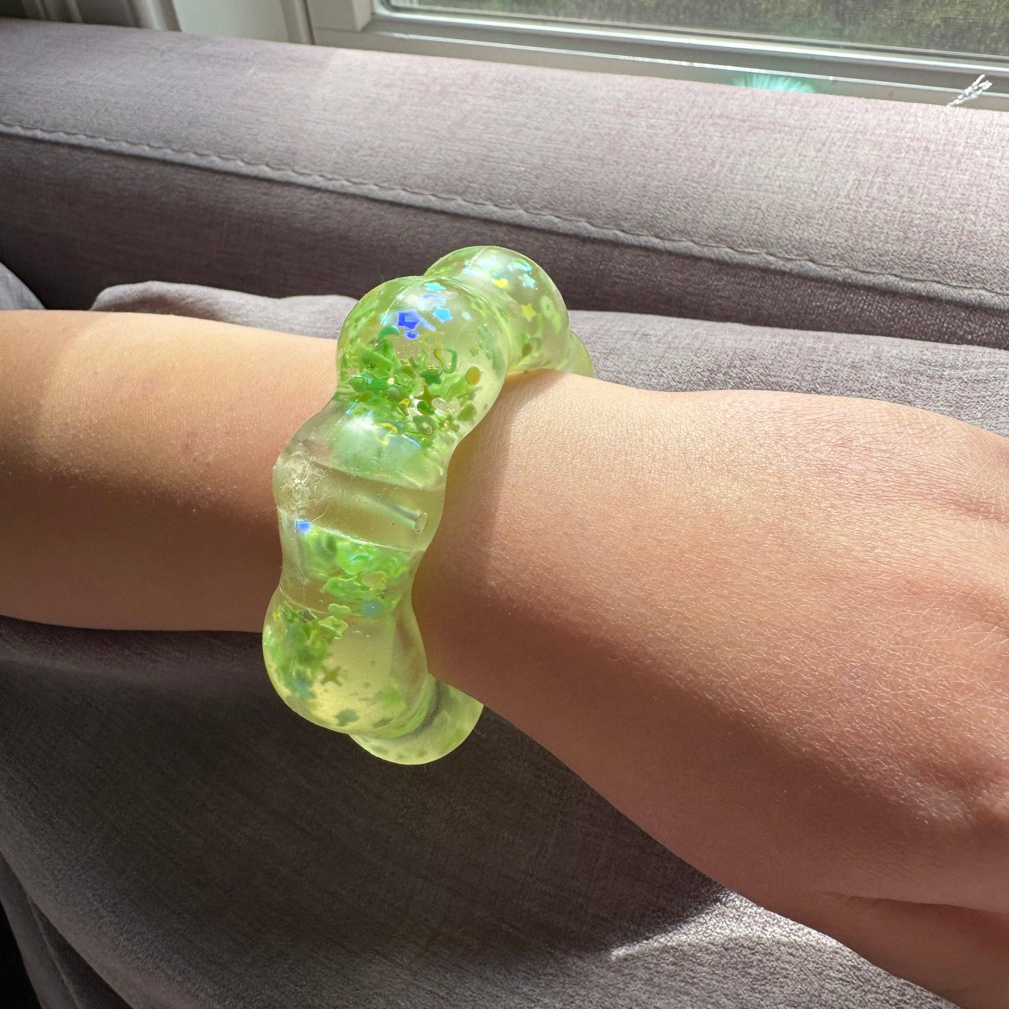 Person wearing a green gel bracelet on a gray couch with a window in the background