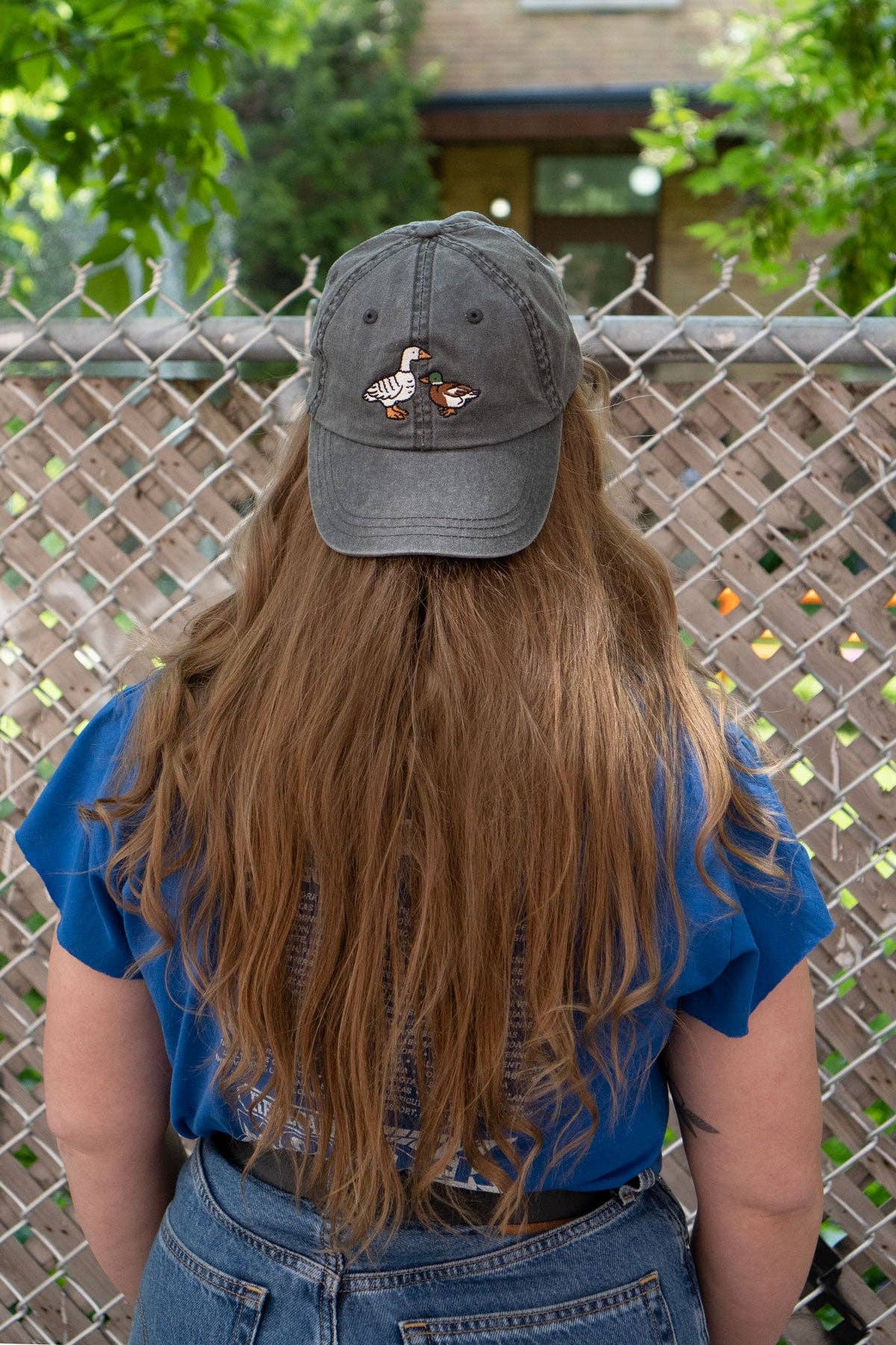 Person wearing a cap with duck design in front of a chain-link fence