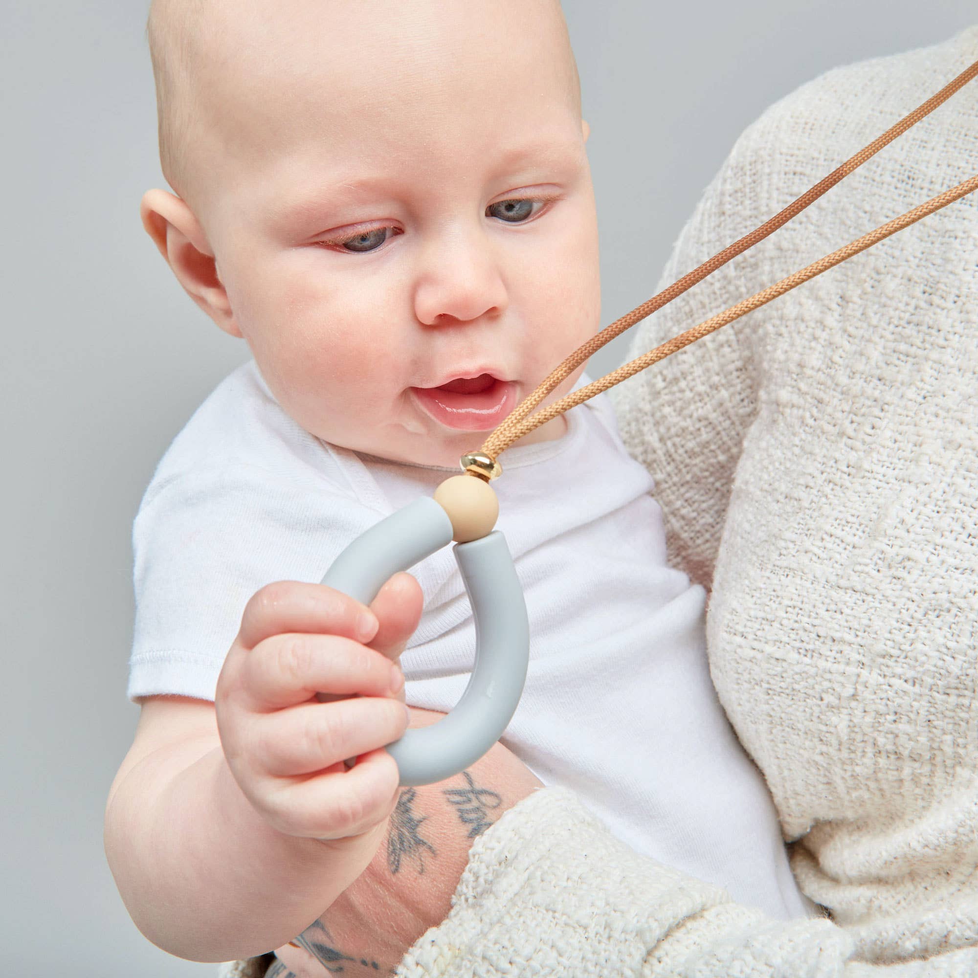 Baby holding a silicone teether with a neutral background
