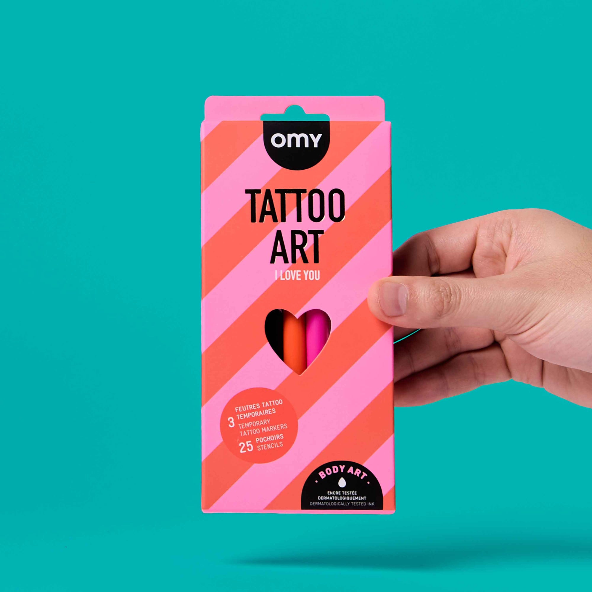 Hand holding a pink and orange 'Tattoo Art' package against a teal background