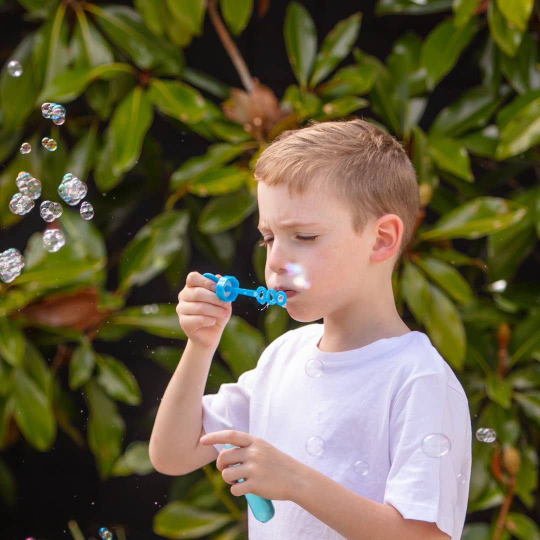 Child blowing bubbles against a green leafy background
