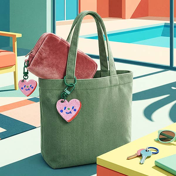 Green tote bag with pink heart-shaped tag on a colorful background