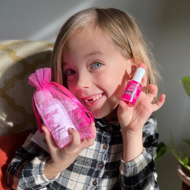 Child holding pink bottles with a checkered shirt and gray pants.