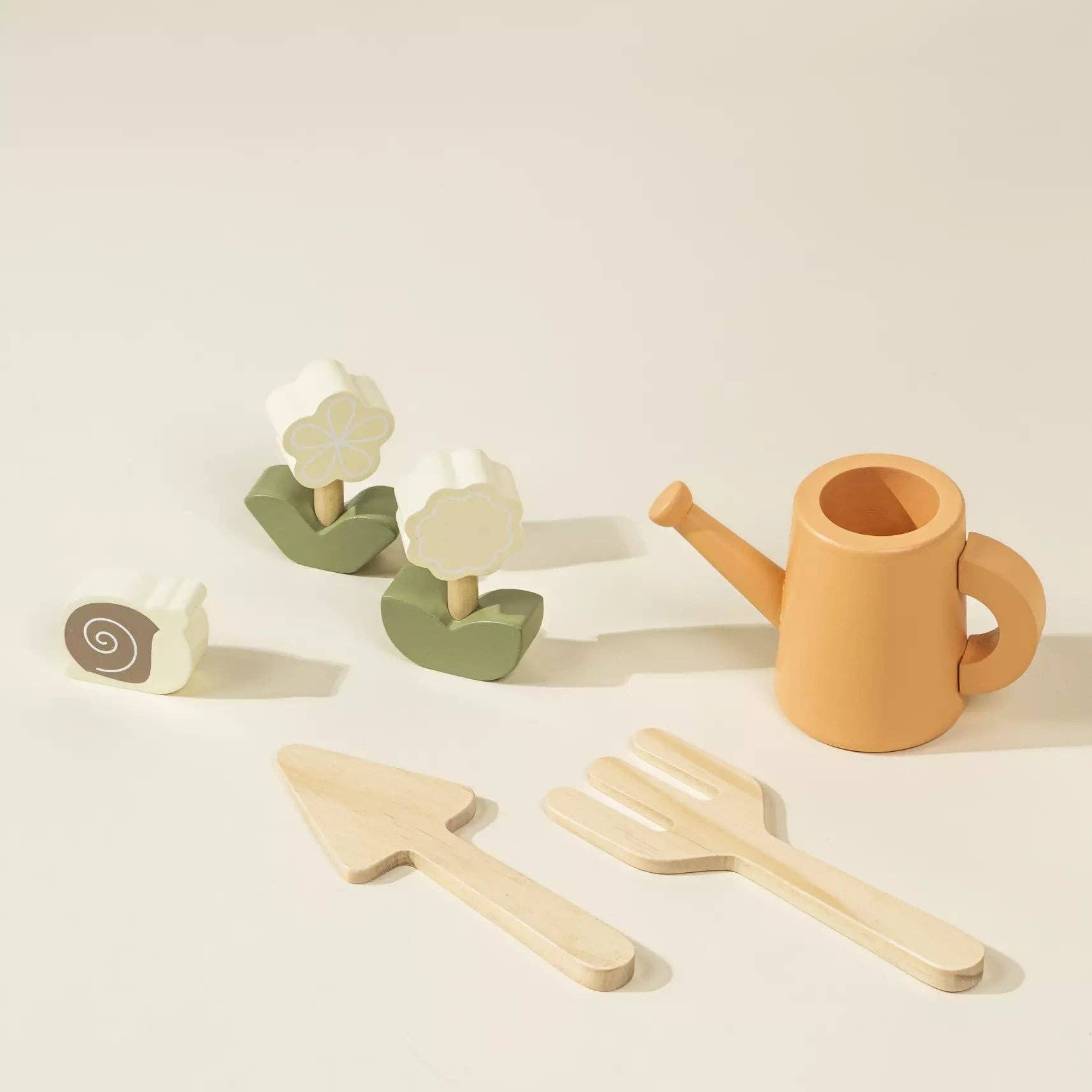 Set of children's gardening toys including a watering can, trowel, and spade on a beige background