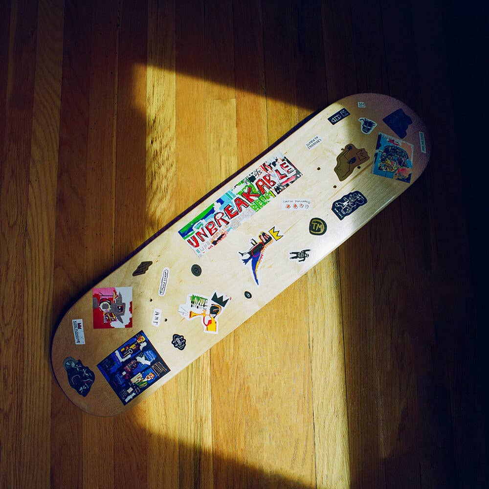 Skateboard deck with various stickers on a wooden floor