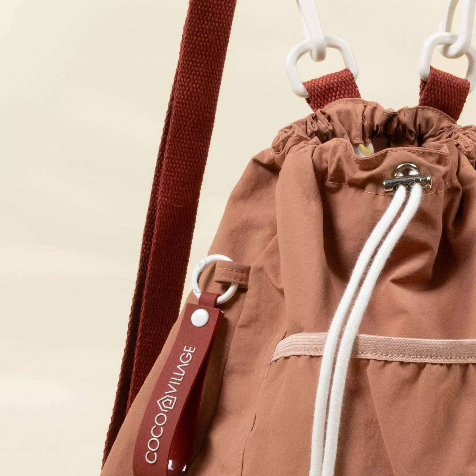 Brown drawstring bag with a red strap and visible brand logo on a beige background