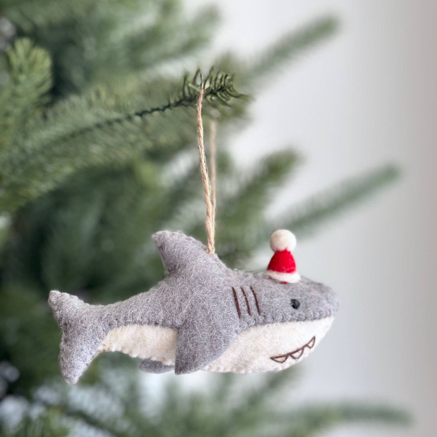 Shark-shaped Christmas ornament with a small figure wearing a Santa hat hanging on a tree.