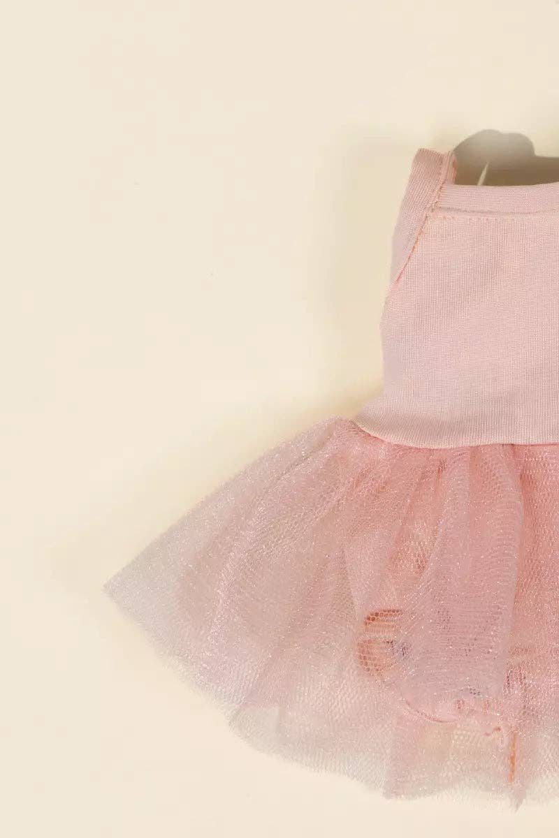 A close-up of a light pink sleeveless dress with a textured bodice and a layered tulle tutu skirt, shown against a plain cream background.