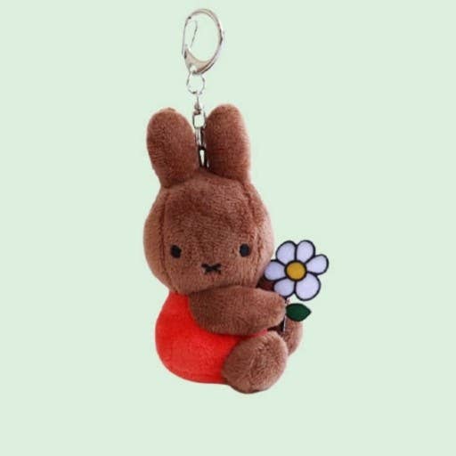 Plush keychain of a brown bunny holding a flower on a light green background