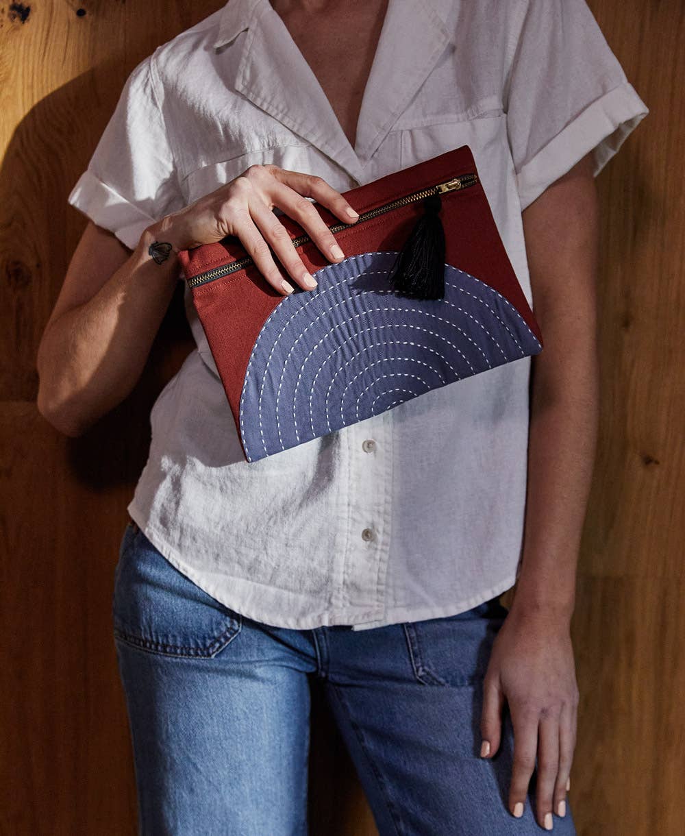 Person holding a red and blue handbag against a wooden background