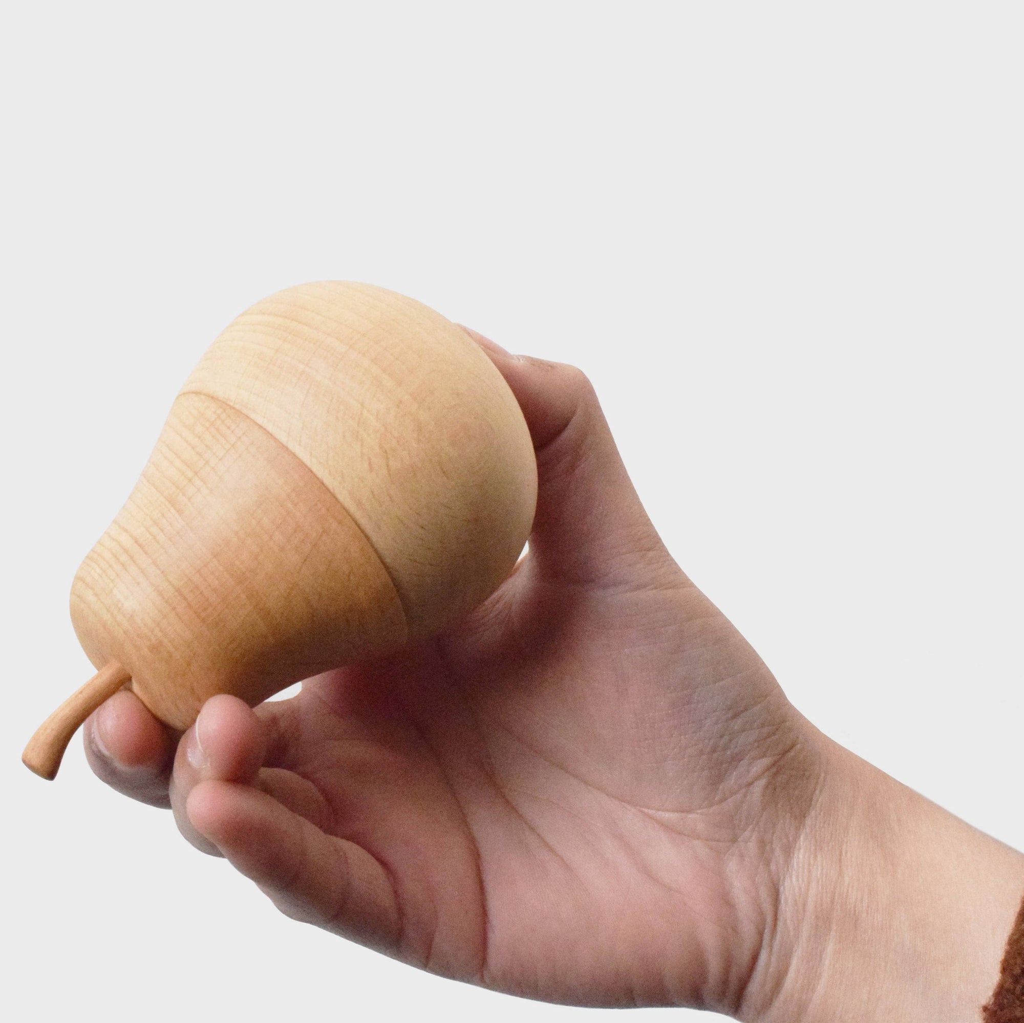 Wooden pear-shaped object held in a hand against a white background