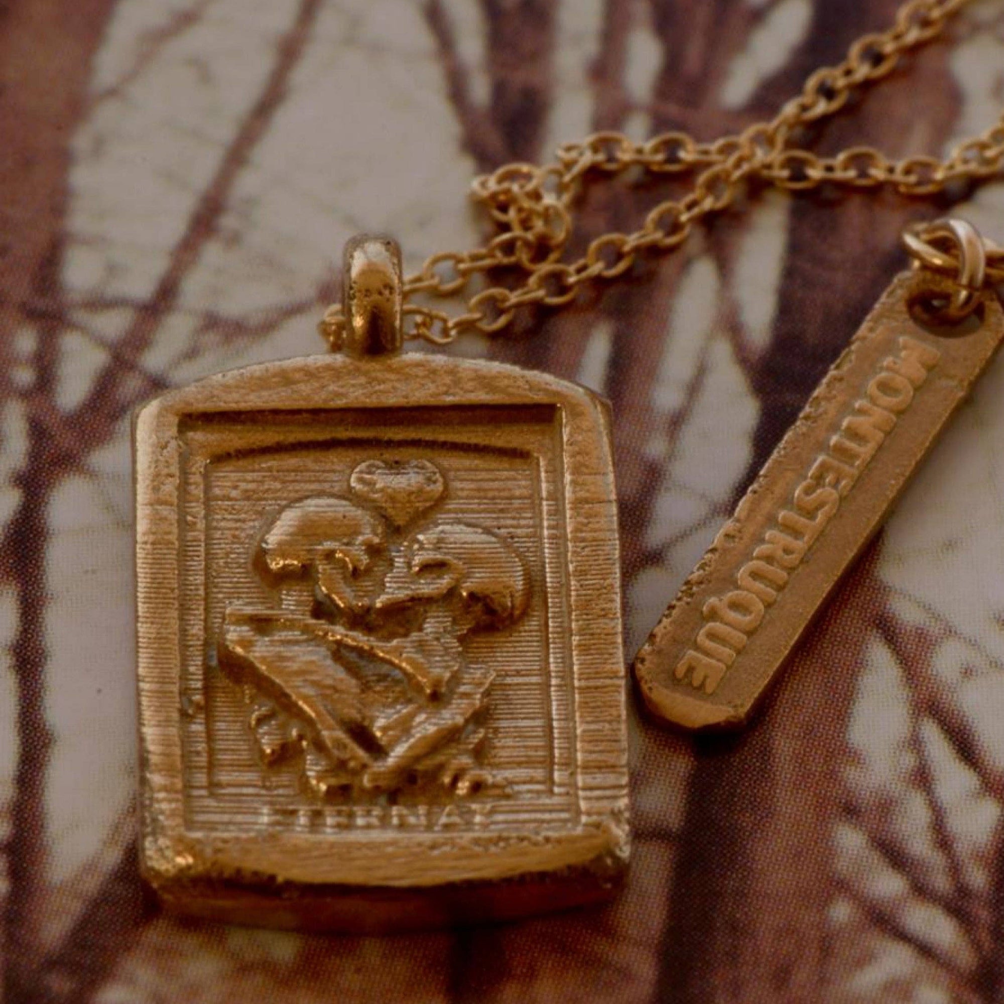 Gold pendant necklace with engraved design on a textured brown background