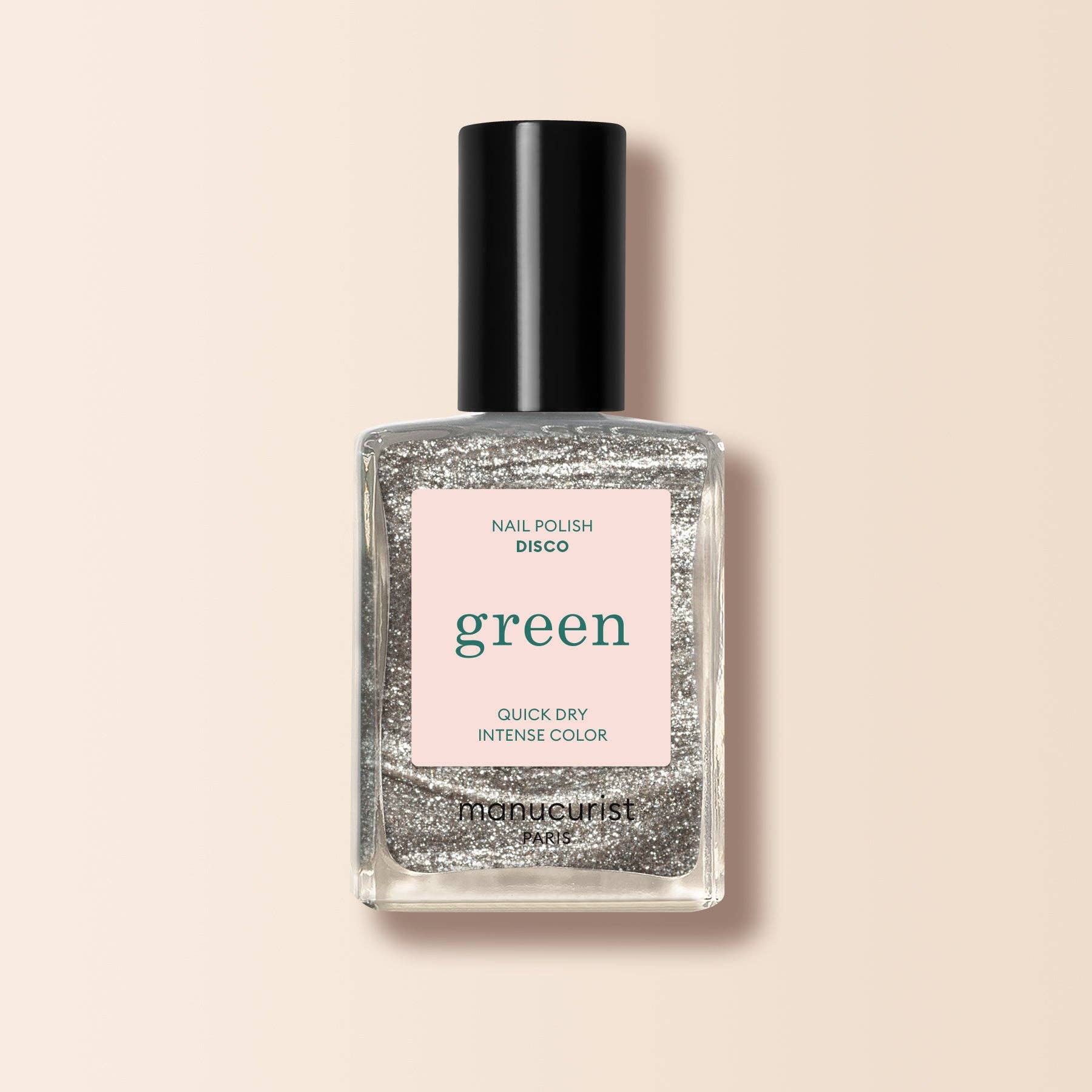 A bottle of Monocurist nail polish in the shade 'green', featuring a black cap and a light pink label, filled with silver glitter polish, set against a solid pale peach background.