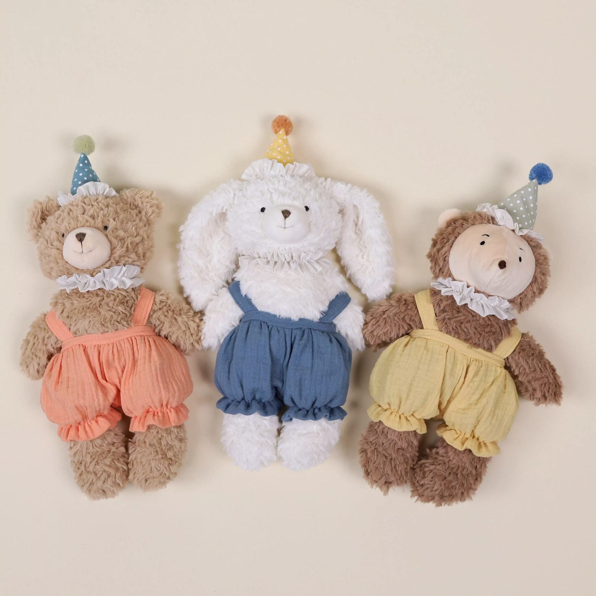 Three stuffed animals, a bear, a rabbit, and a lion, wearing colorful overalls on a beige background.