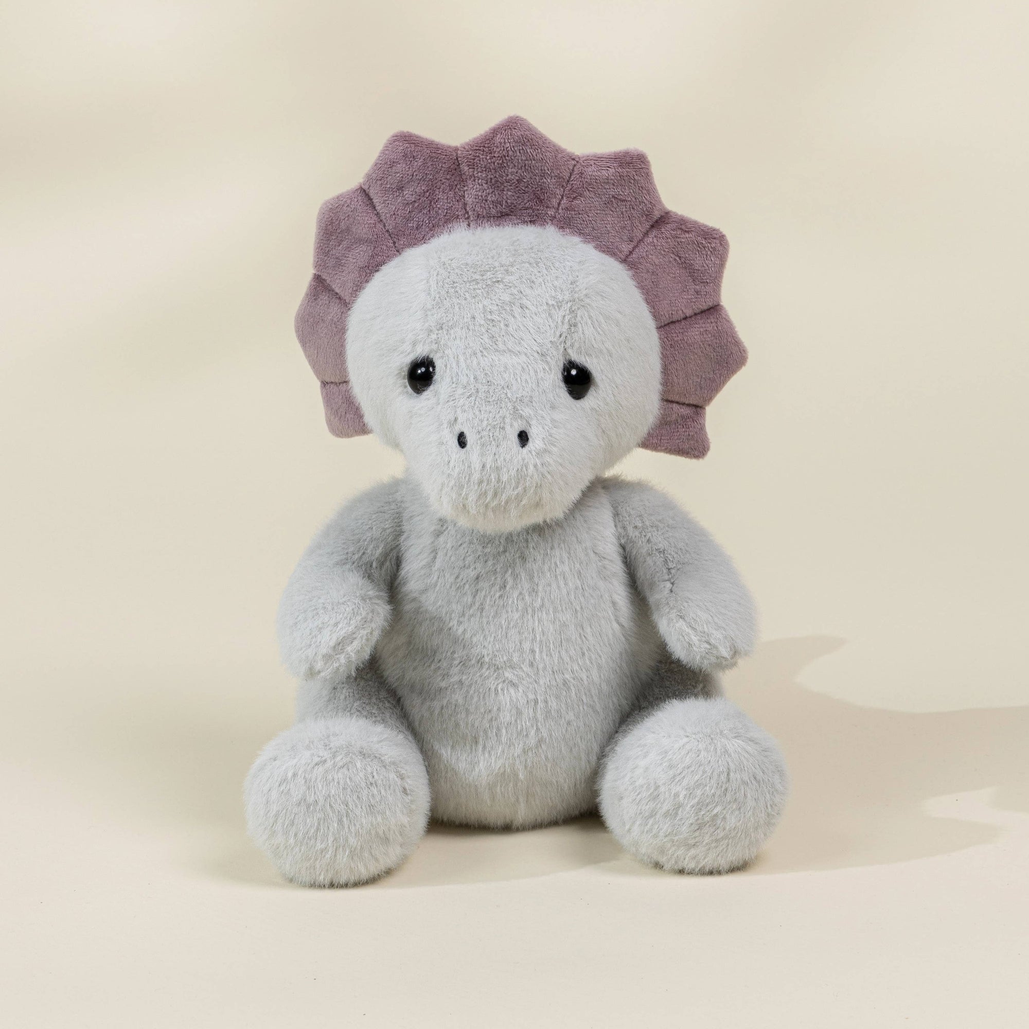 Plush toy dinosaur with a purple frill on a beige background