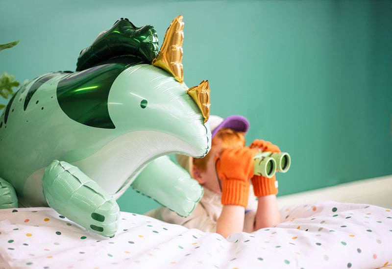 Child playing with a dinosaur-shaped inflatable toy on a bed.