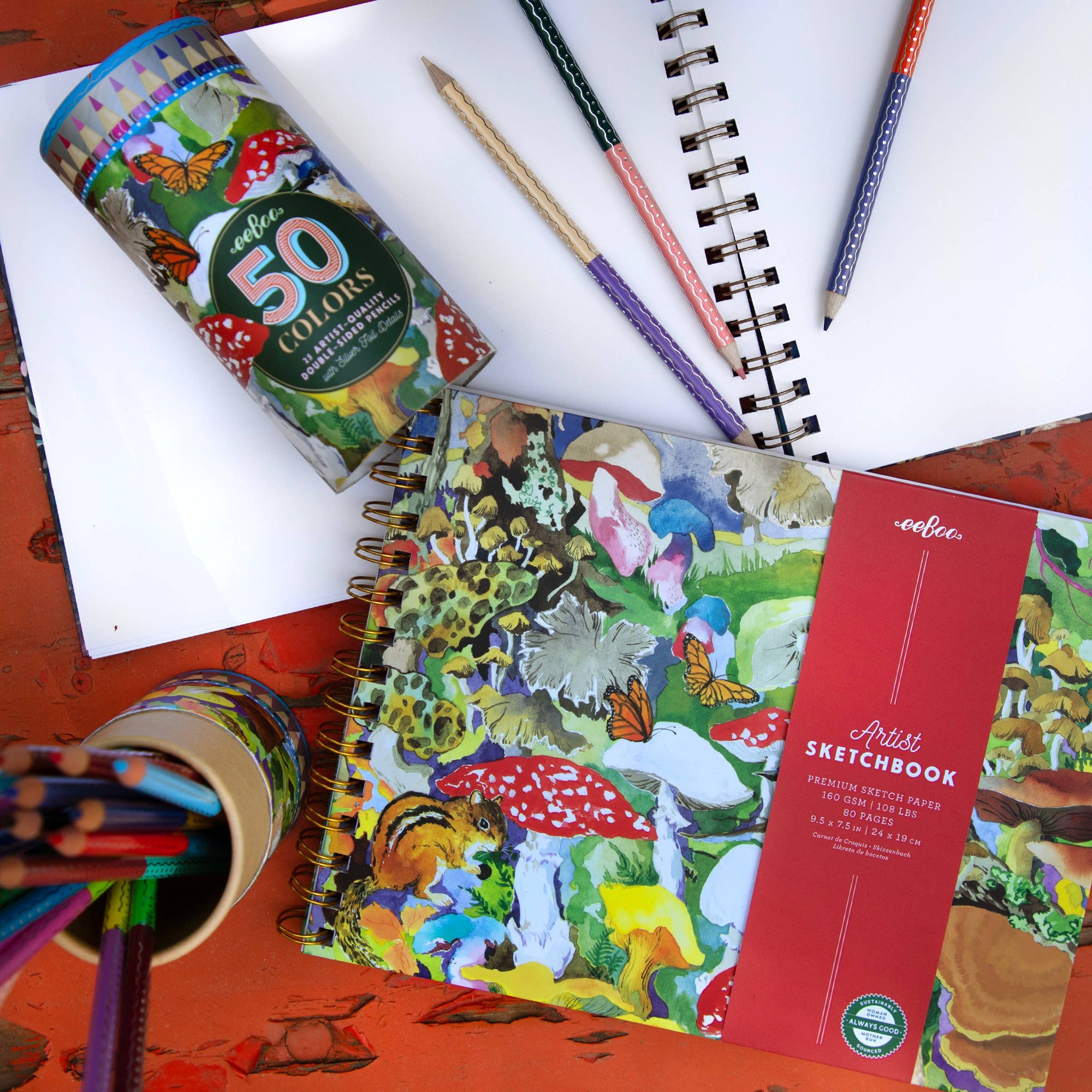 Colorful art supplies including a sketchbook, pencils, and a tube of colored pencils on a white surface.