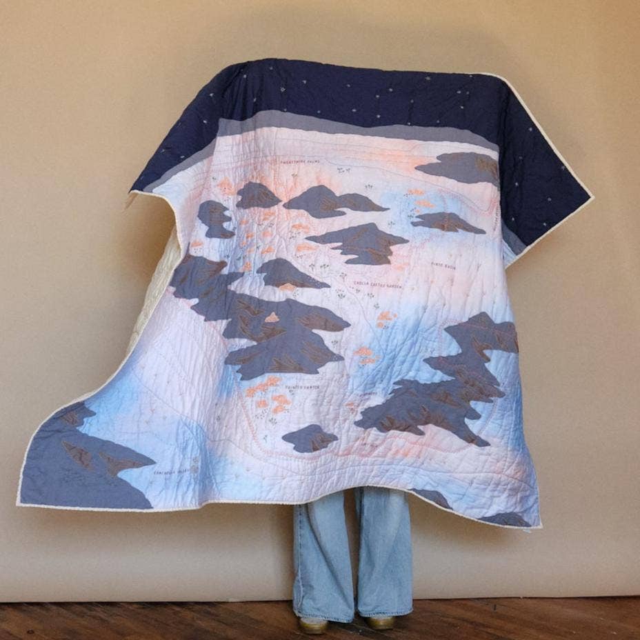 Person wearing a quilt with a mountain design against a beige wall