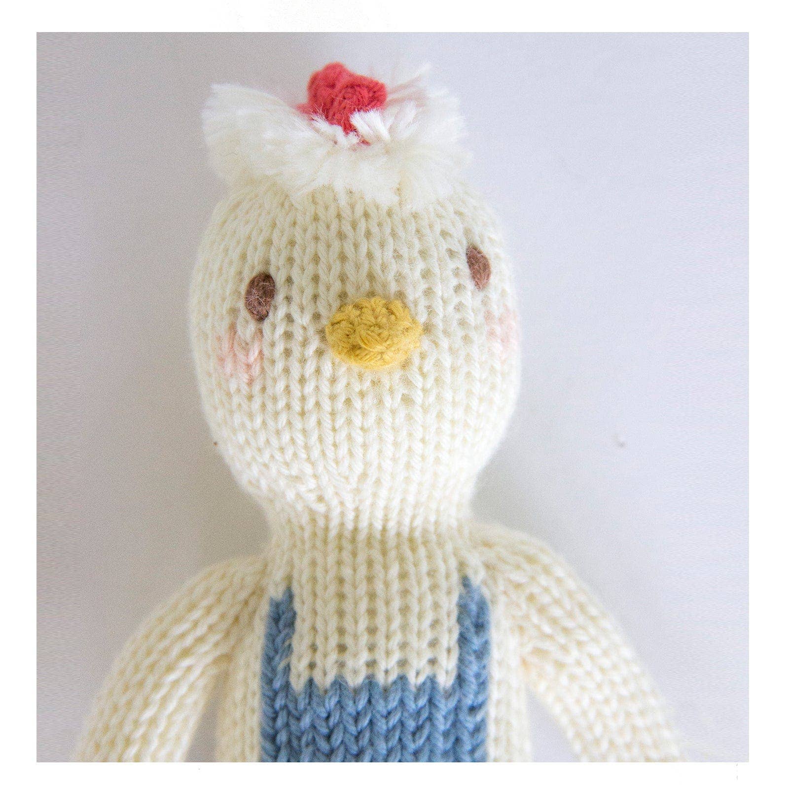Knitted chicken toy with a red comb on a light gray background