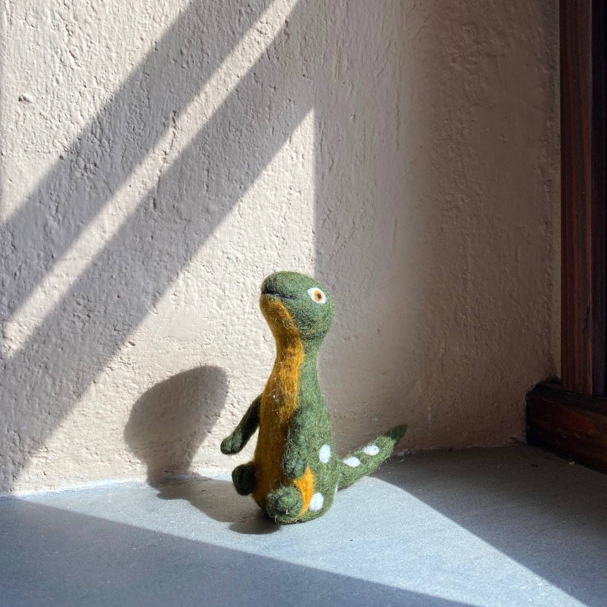 Small green dinosaur toy on a textured surface with sunlight casting shadows